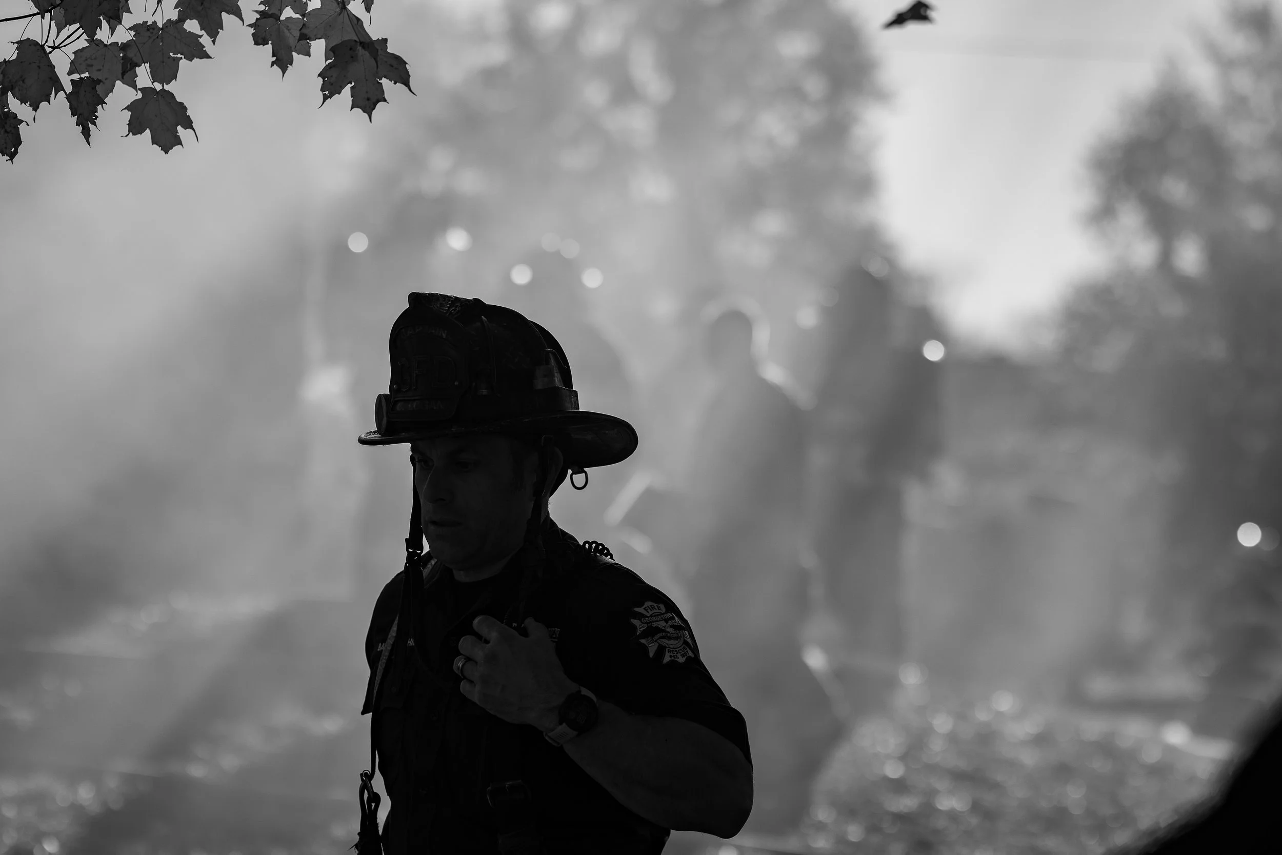 Firefighter wearing a helmet and uniform, with smoke in the background.