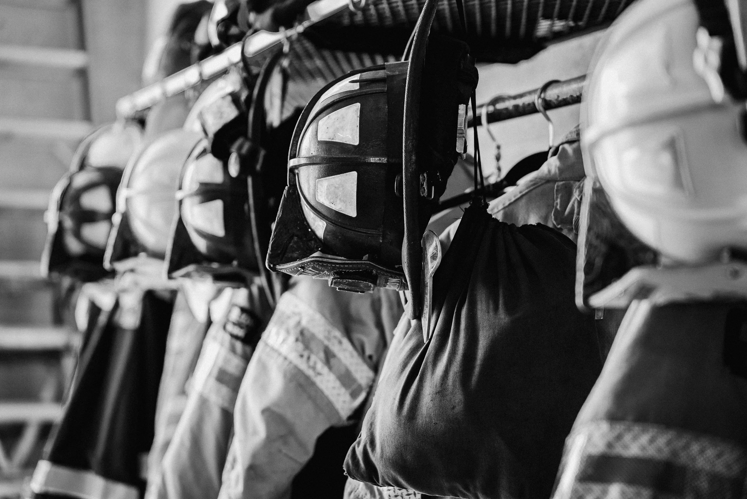 A row of firefighter helmets and gear hanging on a wall, black and white photo.