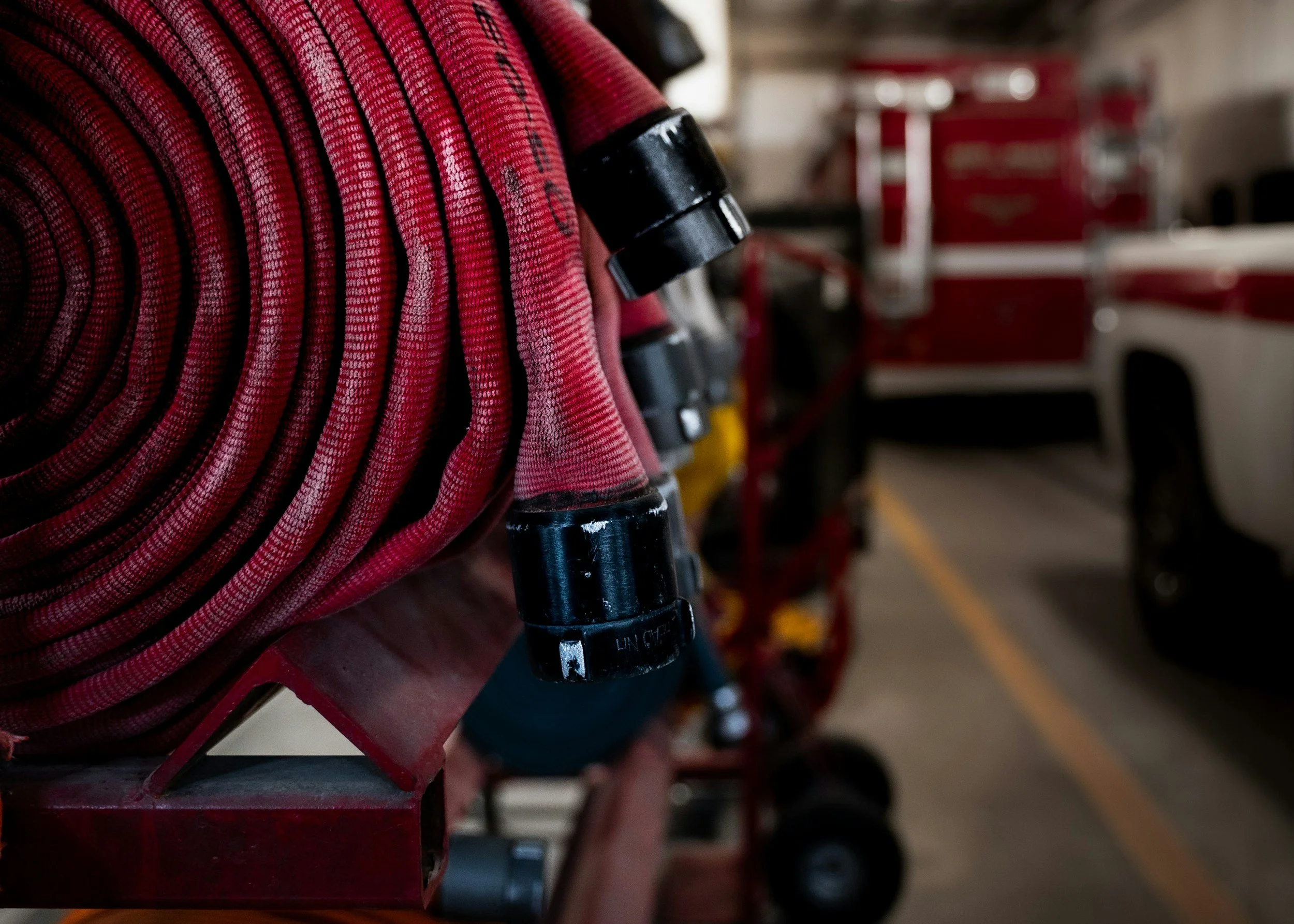 Close-up of a red fire hose reel in a fire station with a vehicle and equipment in the background.