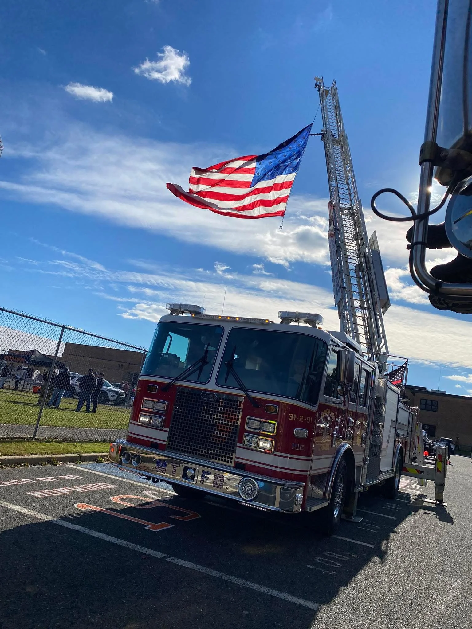American flag flying on a fire truck with an extended ladder, parked outside on a sunny day.