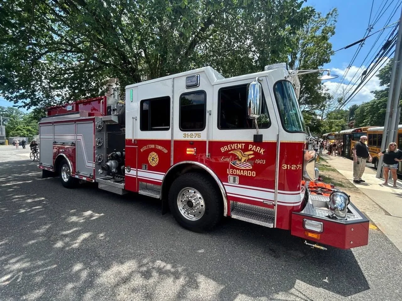 Red and white fire truck with 'Brevent Park,' 'Leonardo,' and 'Middletown Township' written on the side, parked on a street with people and trees around.
