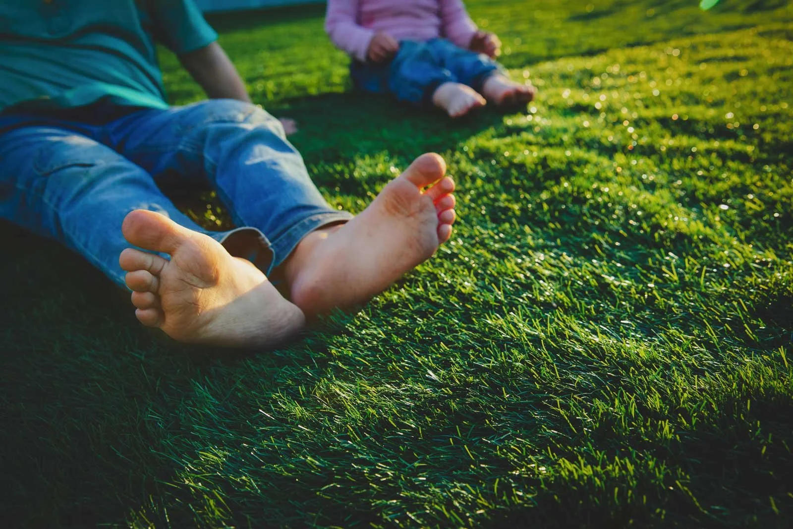 Close-up of children sitting on green grass, with focus on bare feet and legs, enjoying outdoor play.