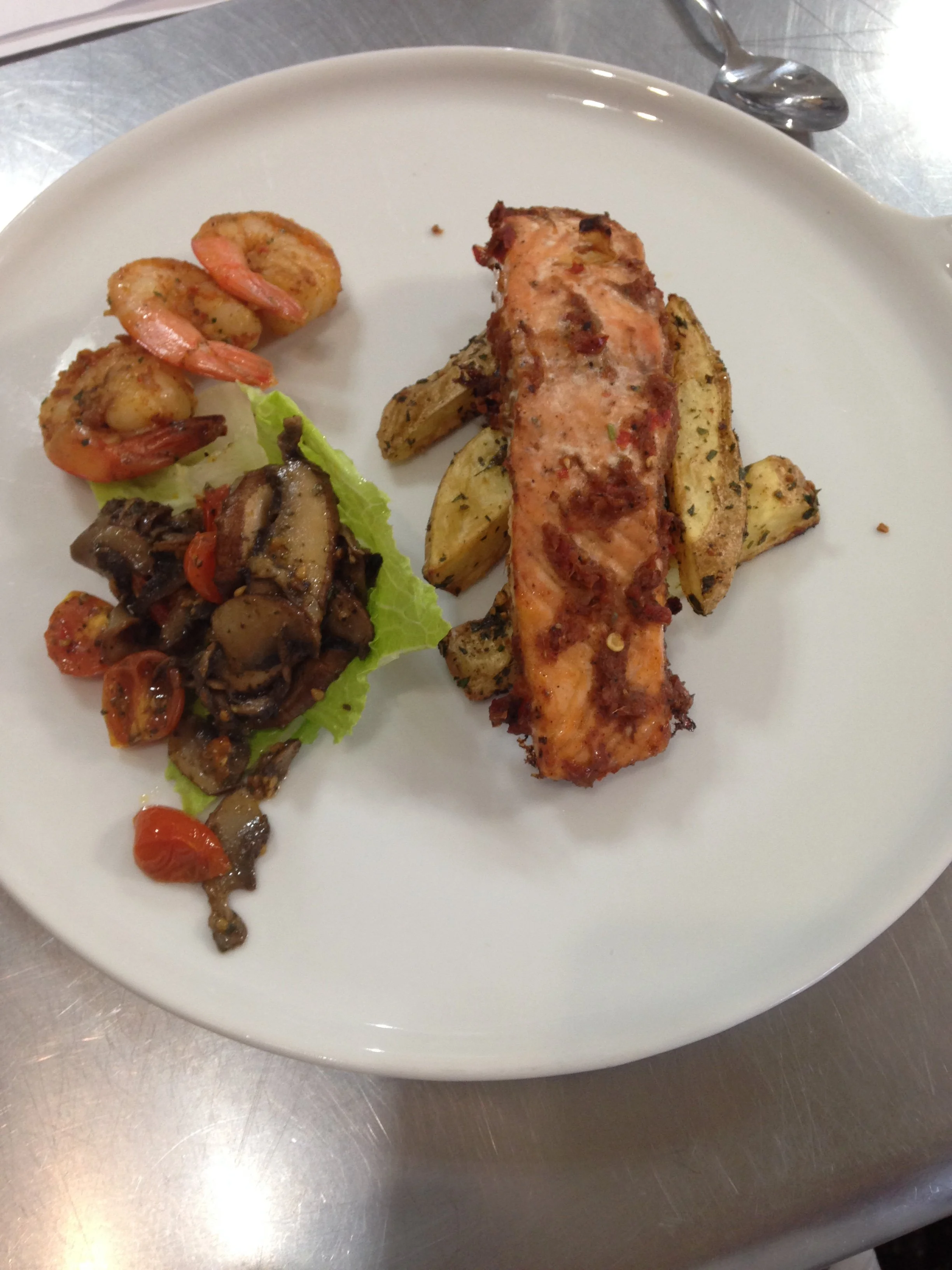Plate with grilled salmon, roasted potatoes, shrimp, and sautéed vegetables.