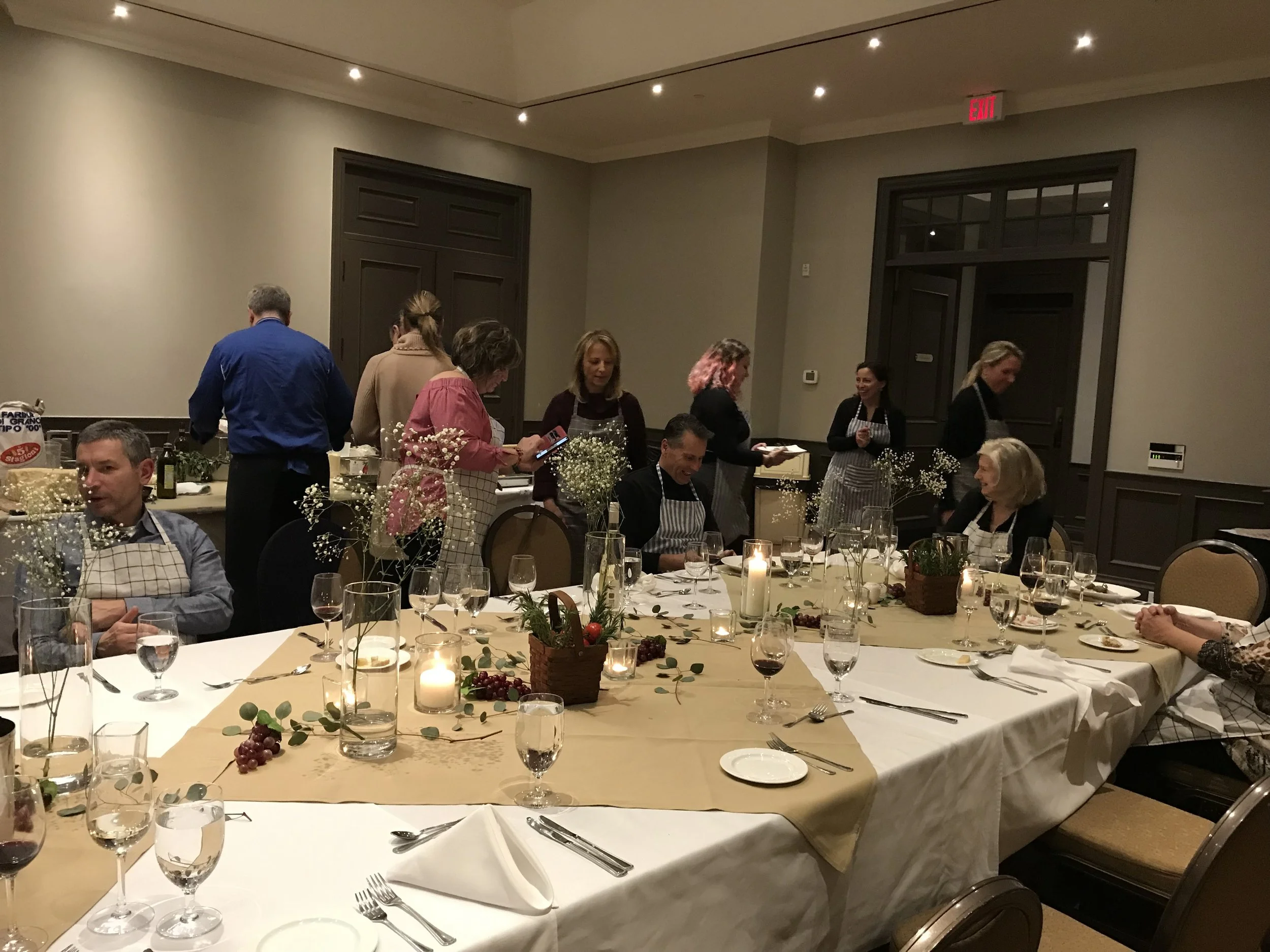 People preparing a banquet table for a meal indoors, with floral decorations and candles