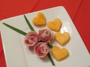 Plate with pink rose-shaped food and yellow heart-shaped cookies or food items, garnished with green leaf-like decorations.