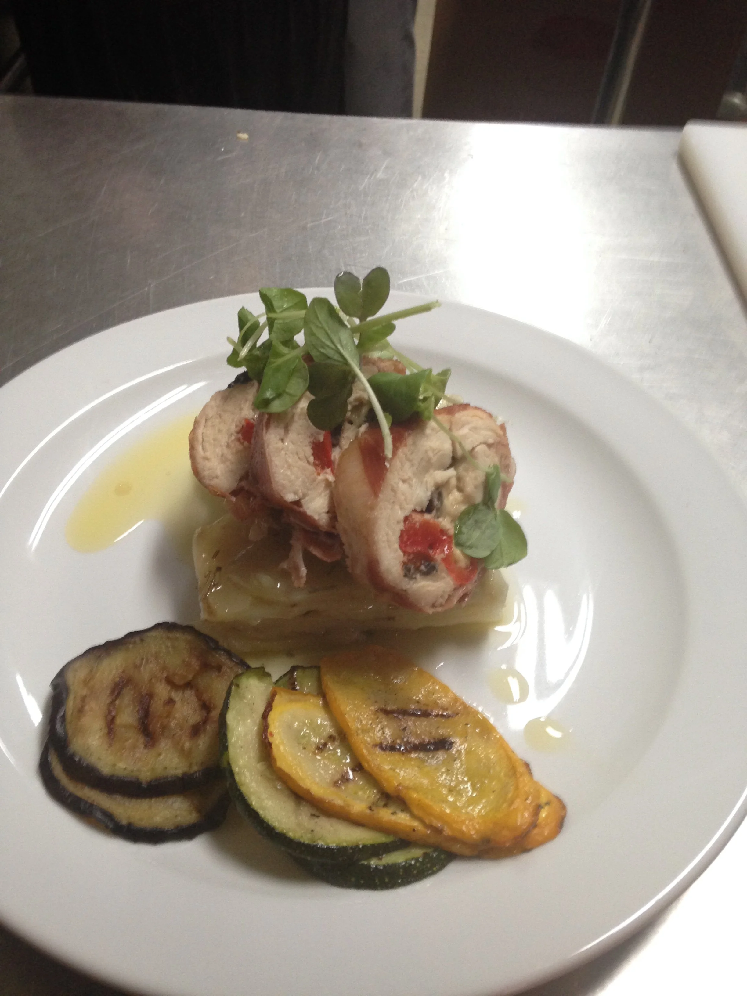A plate of gourmet food with grilled zucchini and yellow squash slices, topped with herbs, and a roulade with a creamy filling garnished with microgreens.