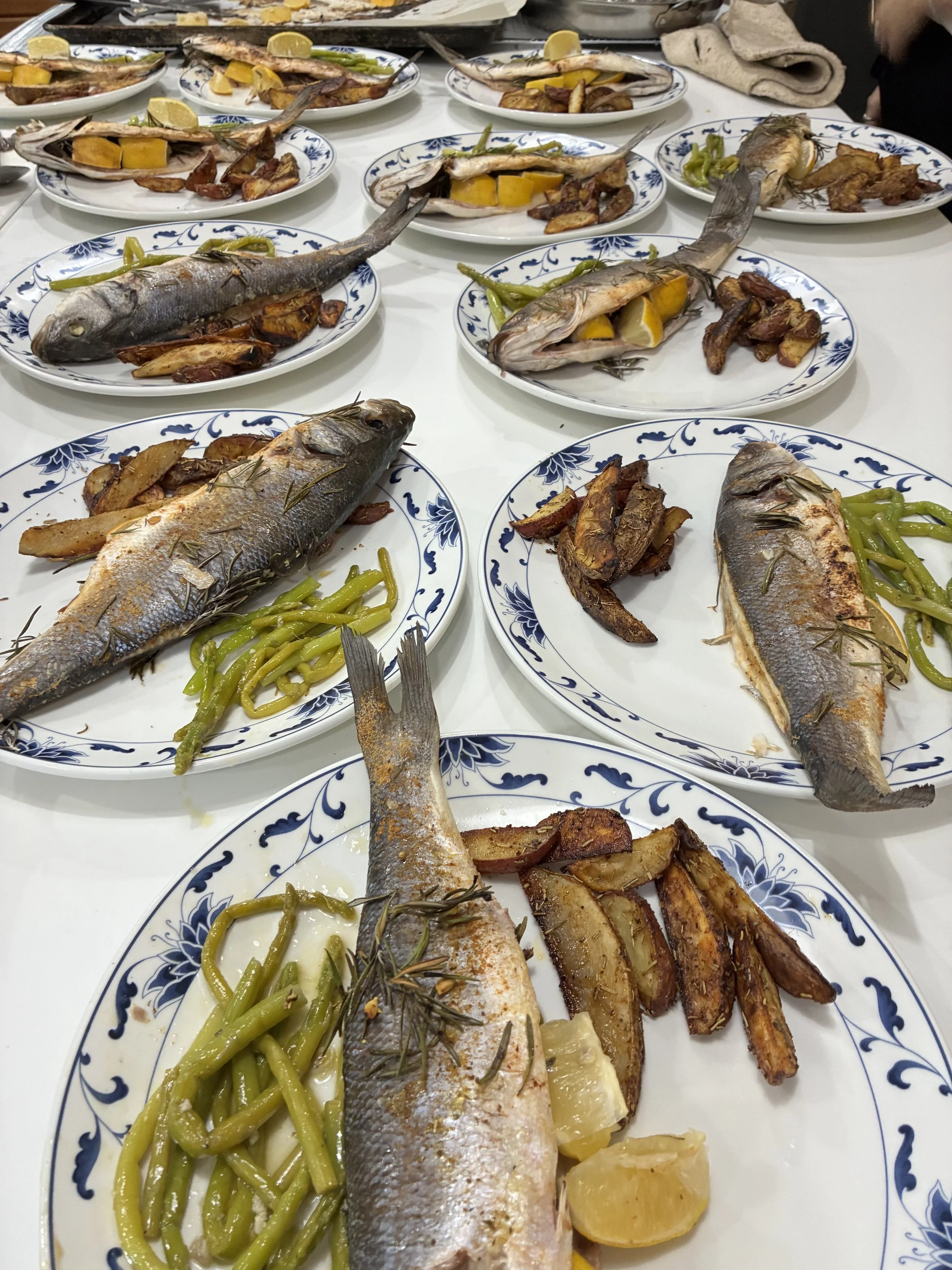 Multiple plates of cooked whole fish with lemon wedges, roasted potatoes, and green beans on a table.