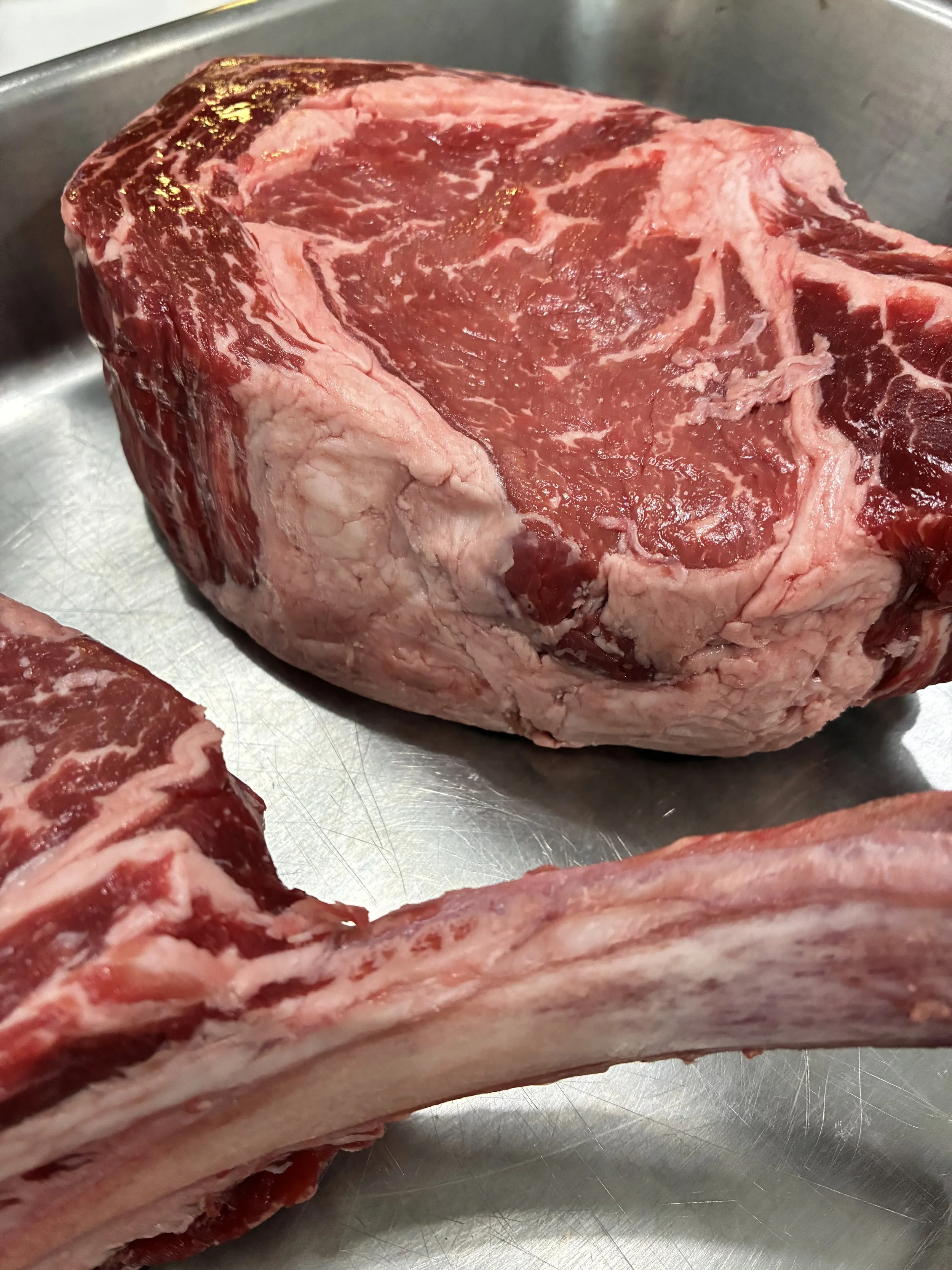 Raw beef with a large cut of meat and a bone on a metal surface.