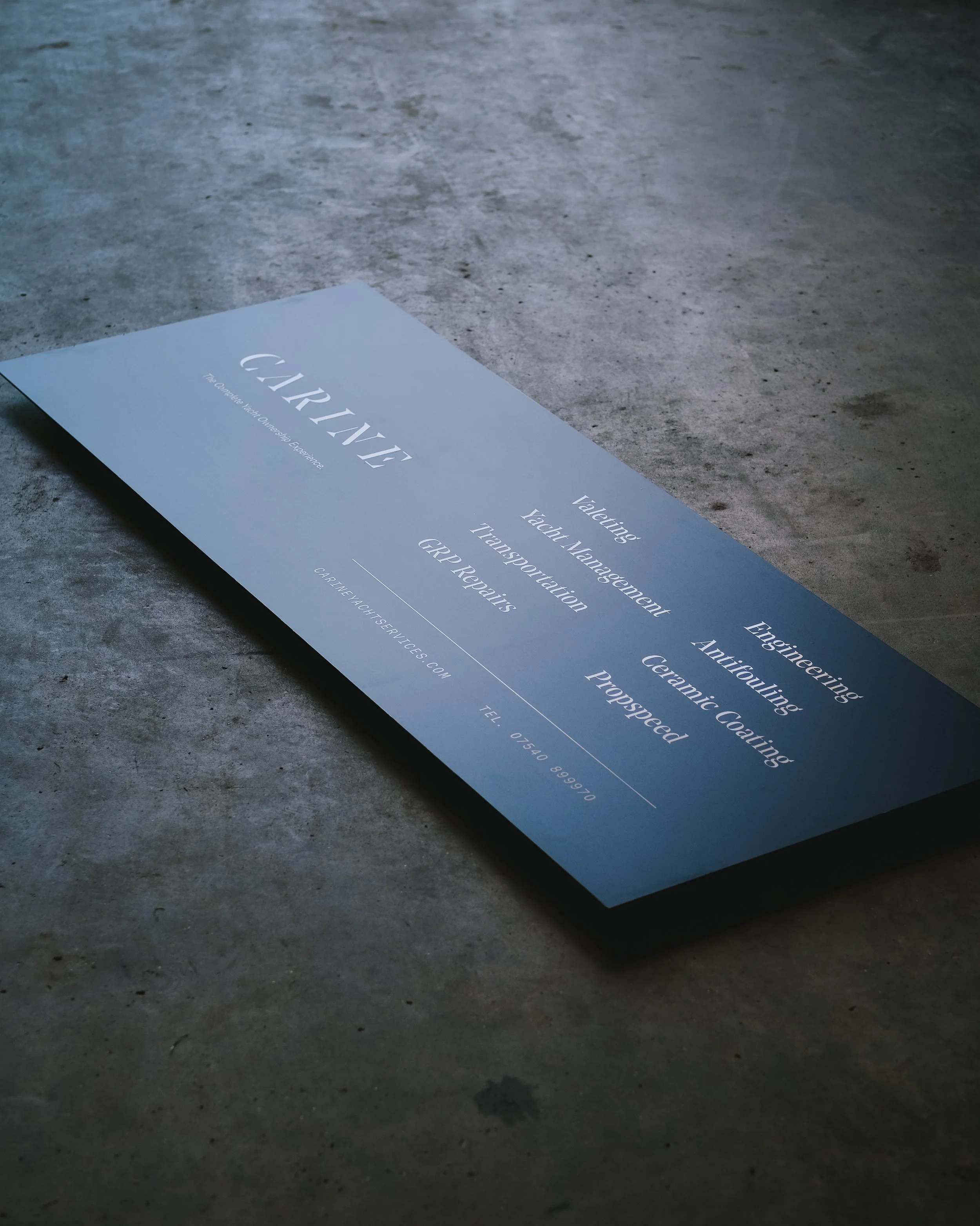 Close-up of a blue business brochure on a concrete surface, featuring text about yacht management, transportation, and GRP repairs.