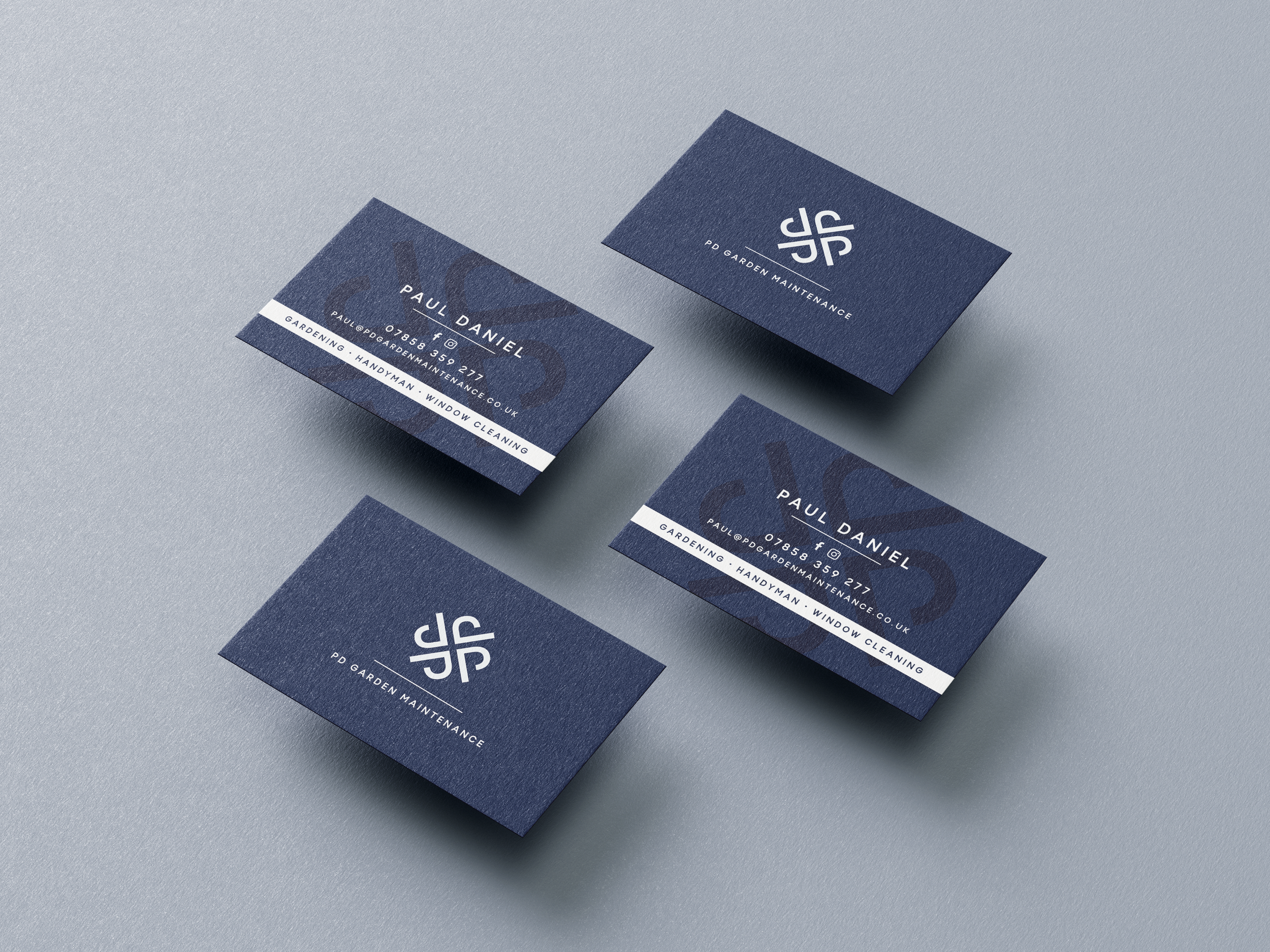 Close-up of dark blue business cards for PD Garden Maintenance, with contact details and logo, on a light gray surface.