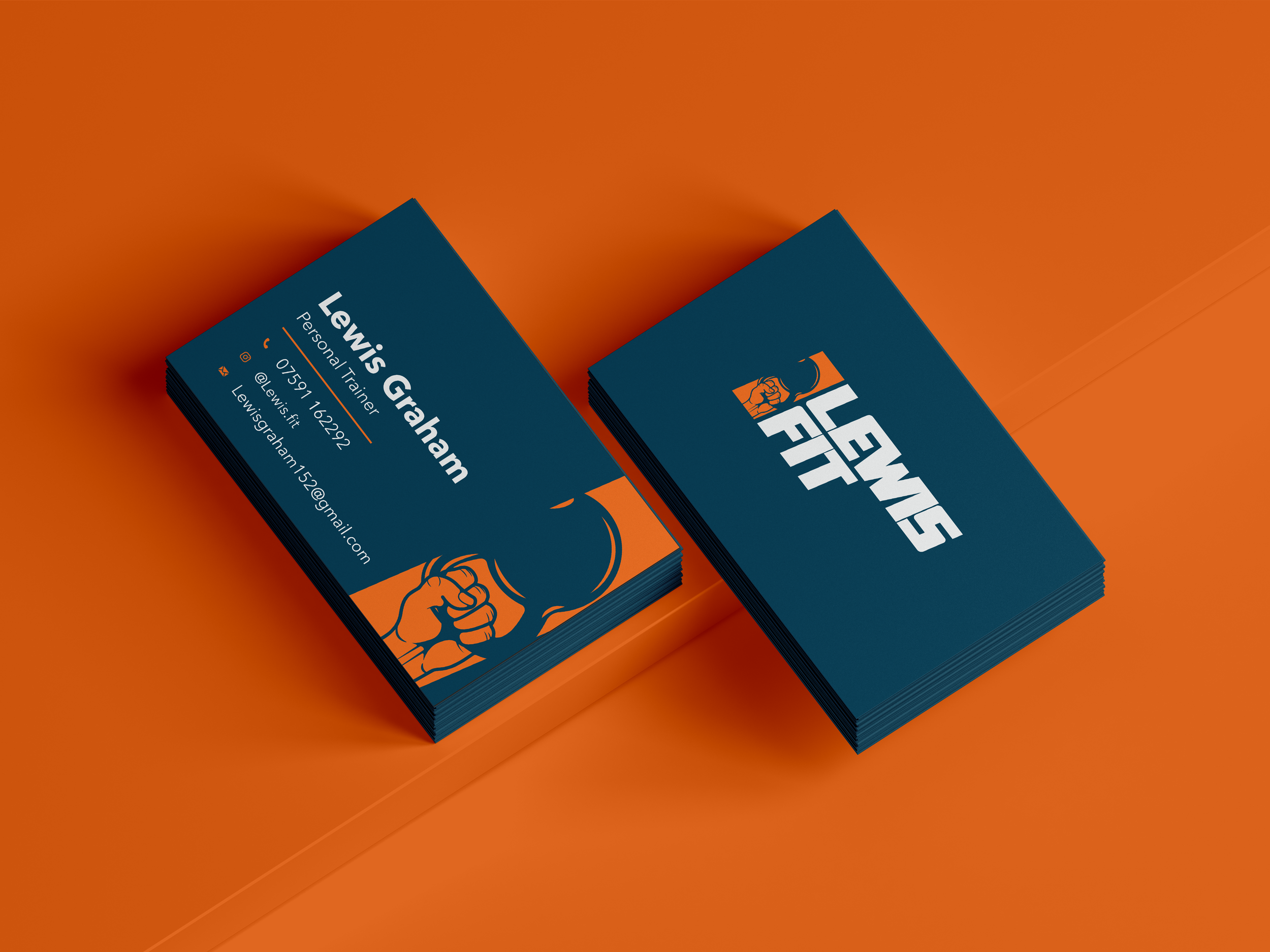 Business cards on an orange surface with a navy blue and orange design. One card displays the name Lewis Graham, contact information, and a logo featuring a clenched fist.