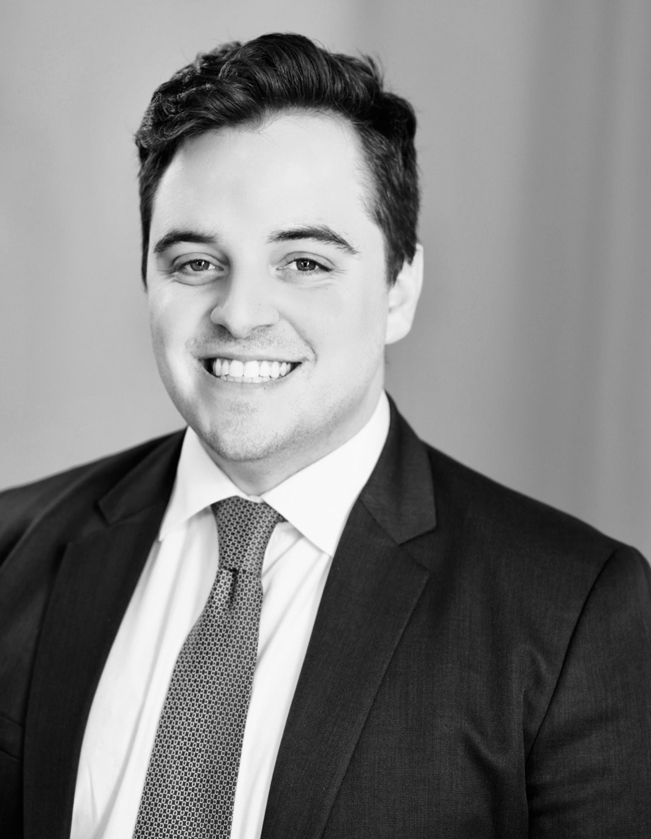 Black-and-white portrait of a young man in a suit and tie, smiling.