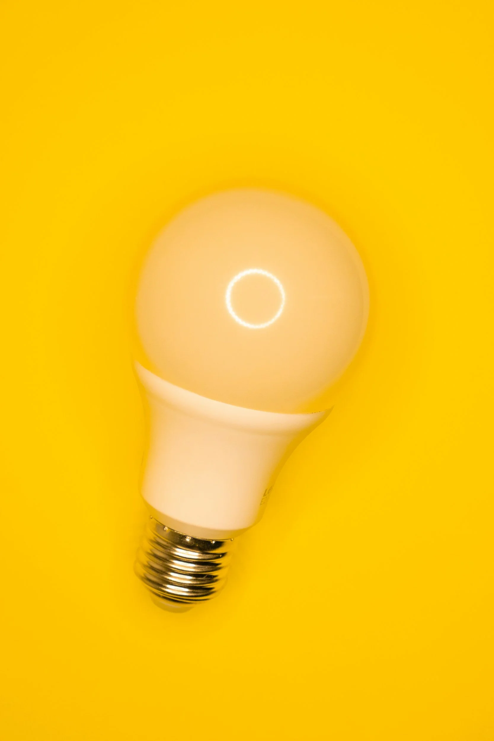 An LED light bulb with a yellow background, glowing with the filament visible inside.