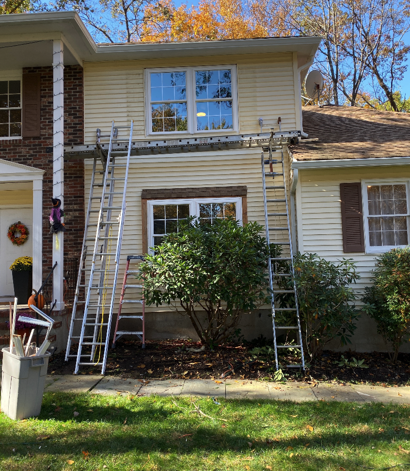 House exterior with construction or maintenance work in progress, ladders propped against the house, and tools in a bin on the grass.