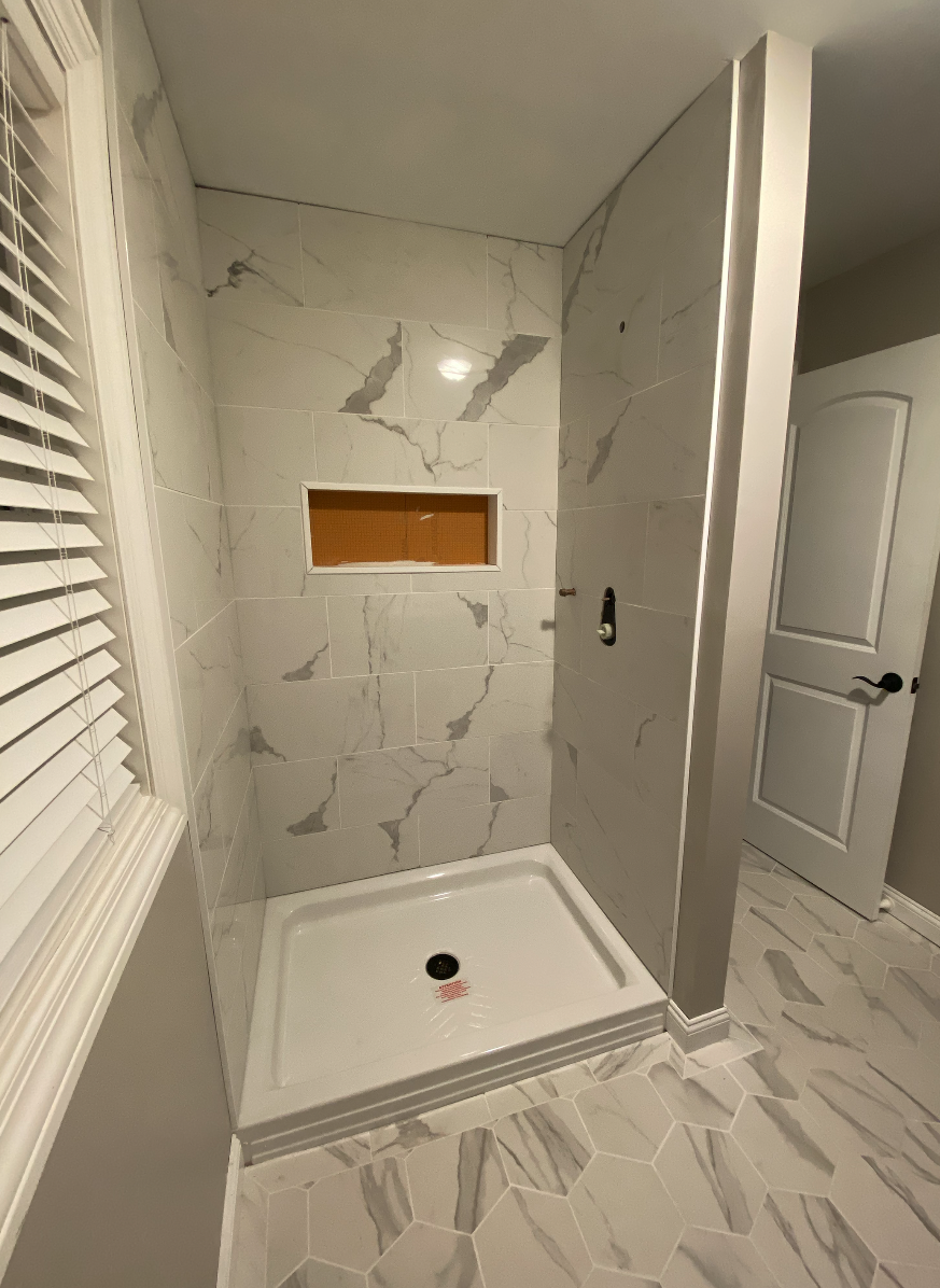 Bathroom Renovation in Morris County NJ. Empty shower stall with white marble tiles, a small built-in shelf, and octagonal floor tiles.