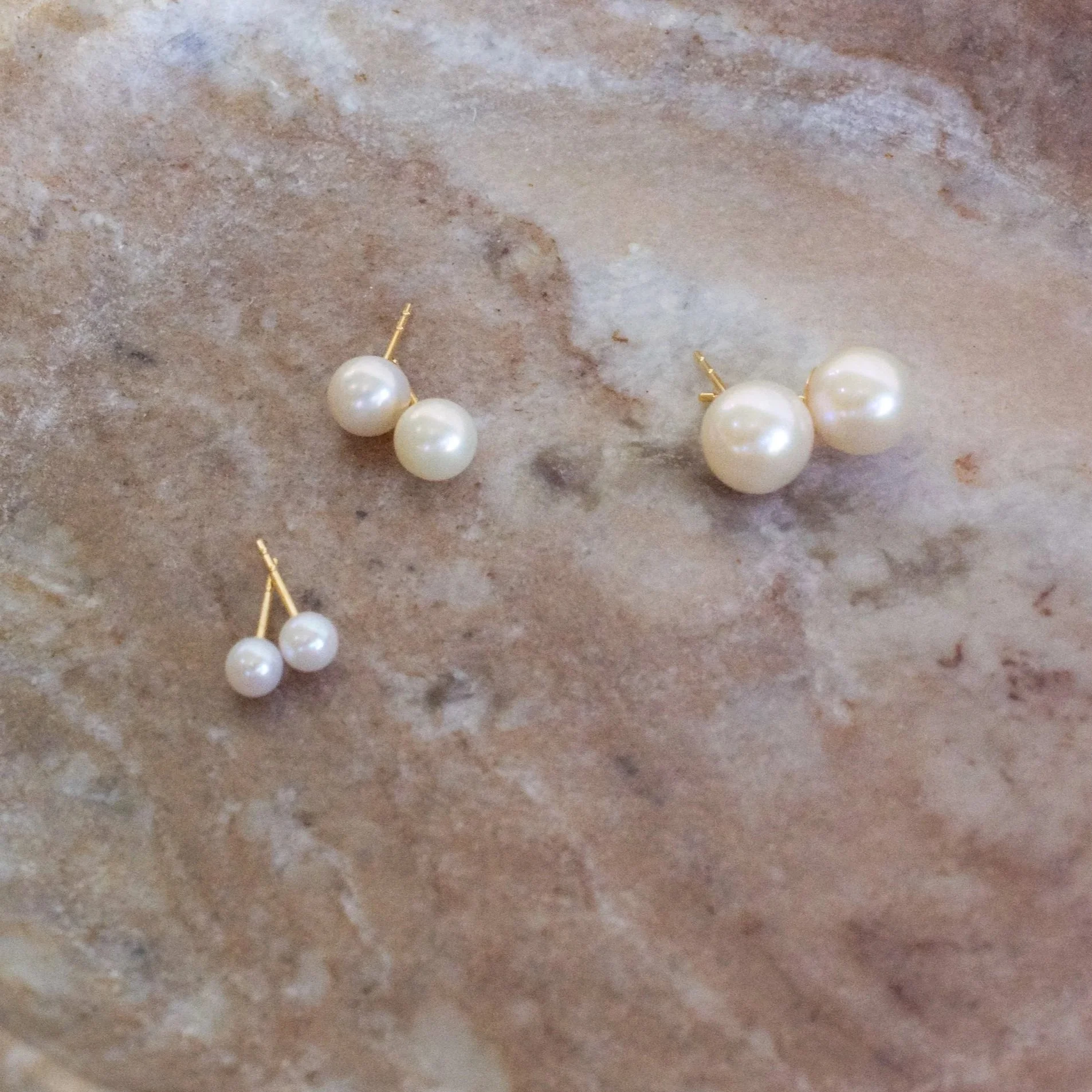 Close-up of pearl earrings with gold posts on a textured surface.