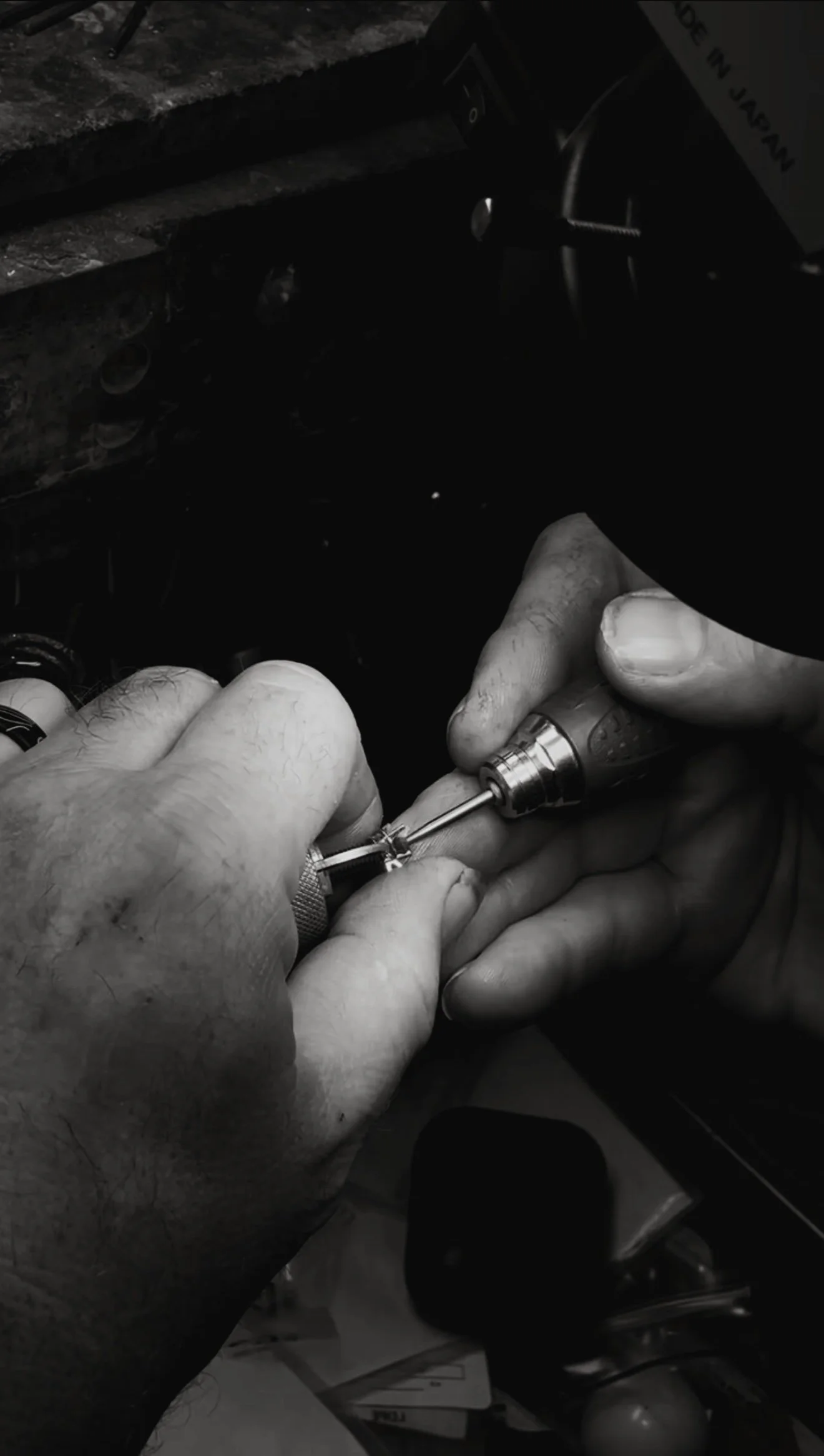 Close-up of hands holding a rotary tool and working on a small object, in a cluttered workspace.