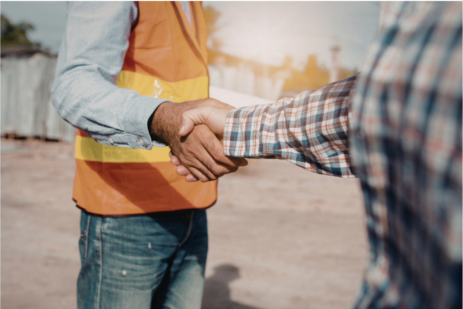 Two individuals shaking hands at a construction site, one wearing a high-visibility safety vest and the other in a plaid shirt.