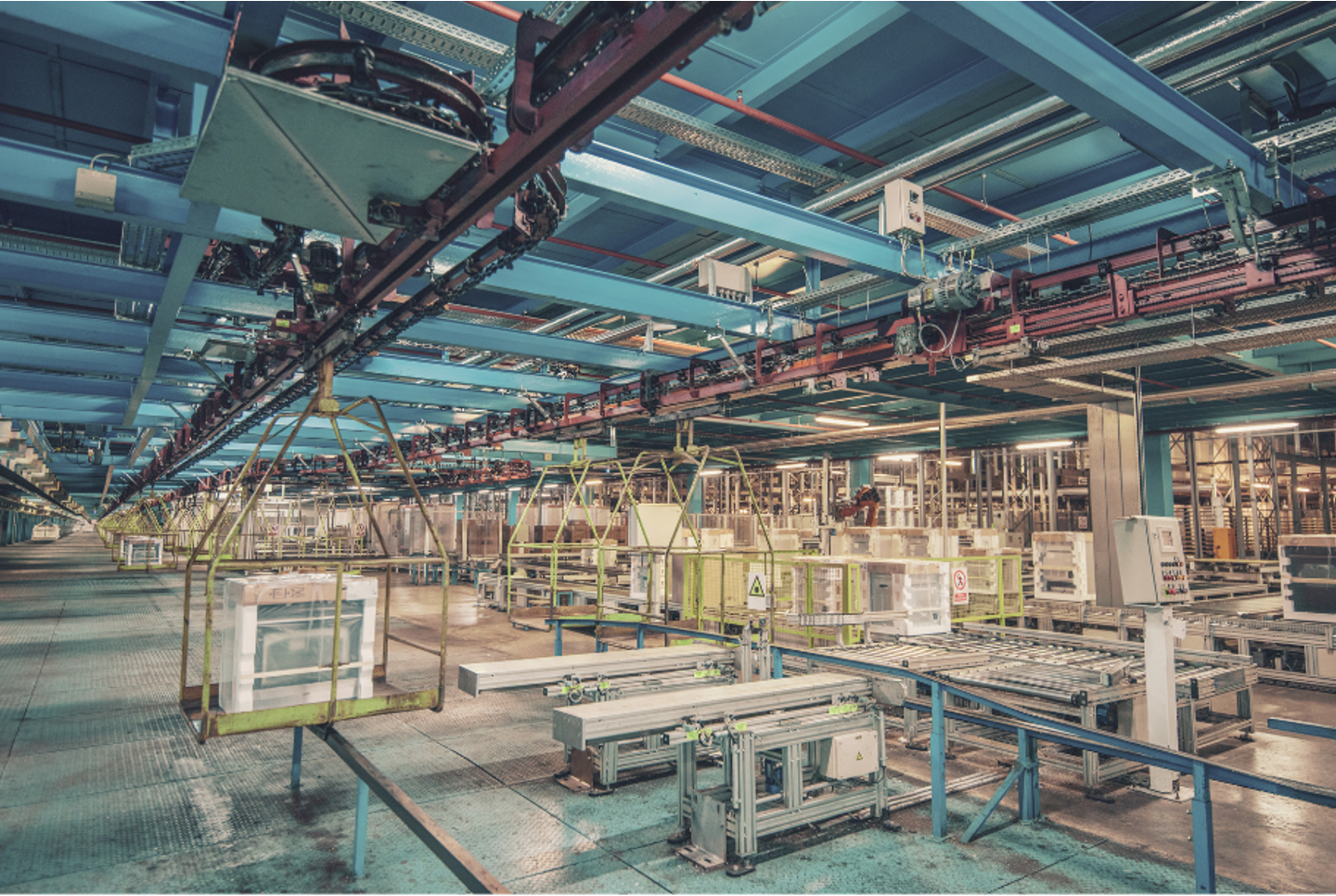 Inside a large manufacturing or industrial facility with conveyor systems, automated machinery, robotic arms, and storage compartments.