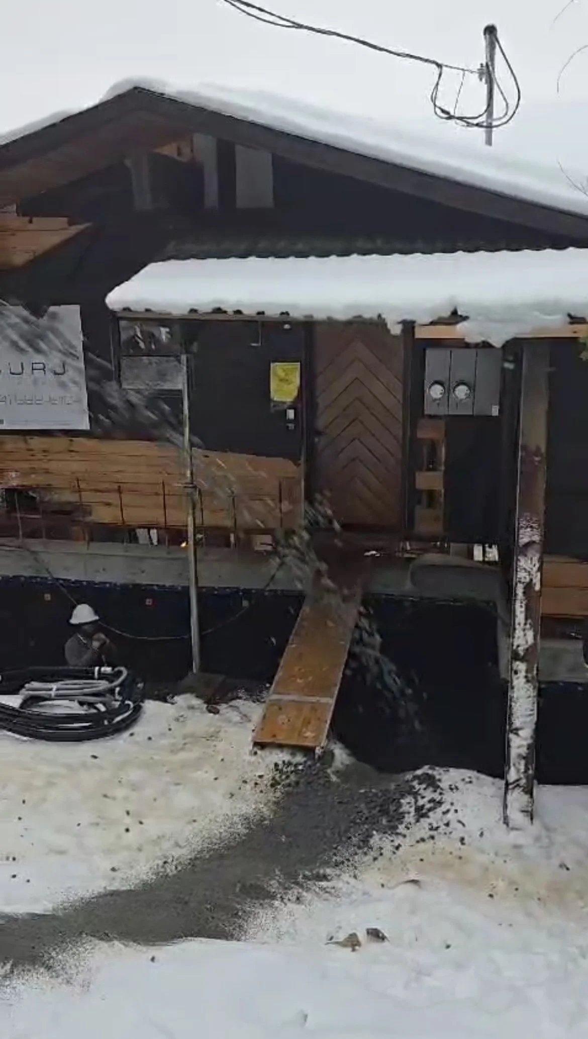 Slinger truck slinging aggregate onto snow-covered ground in front of a building with wood and black exterior wall