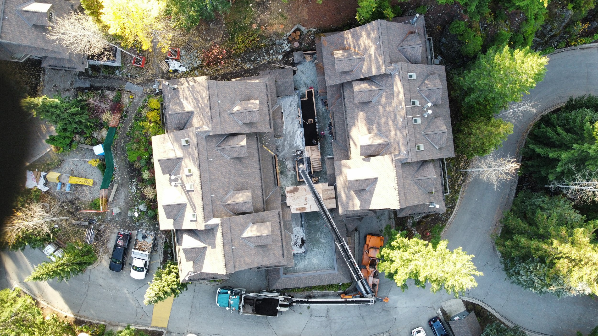 An aerial view of a large building with multiple rooftops surrounded by trees and a curved driveway. Utilising both a stone slinger and conveyor truck to deliver soil to into garden beds with very tight access in Whistler.