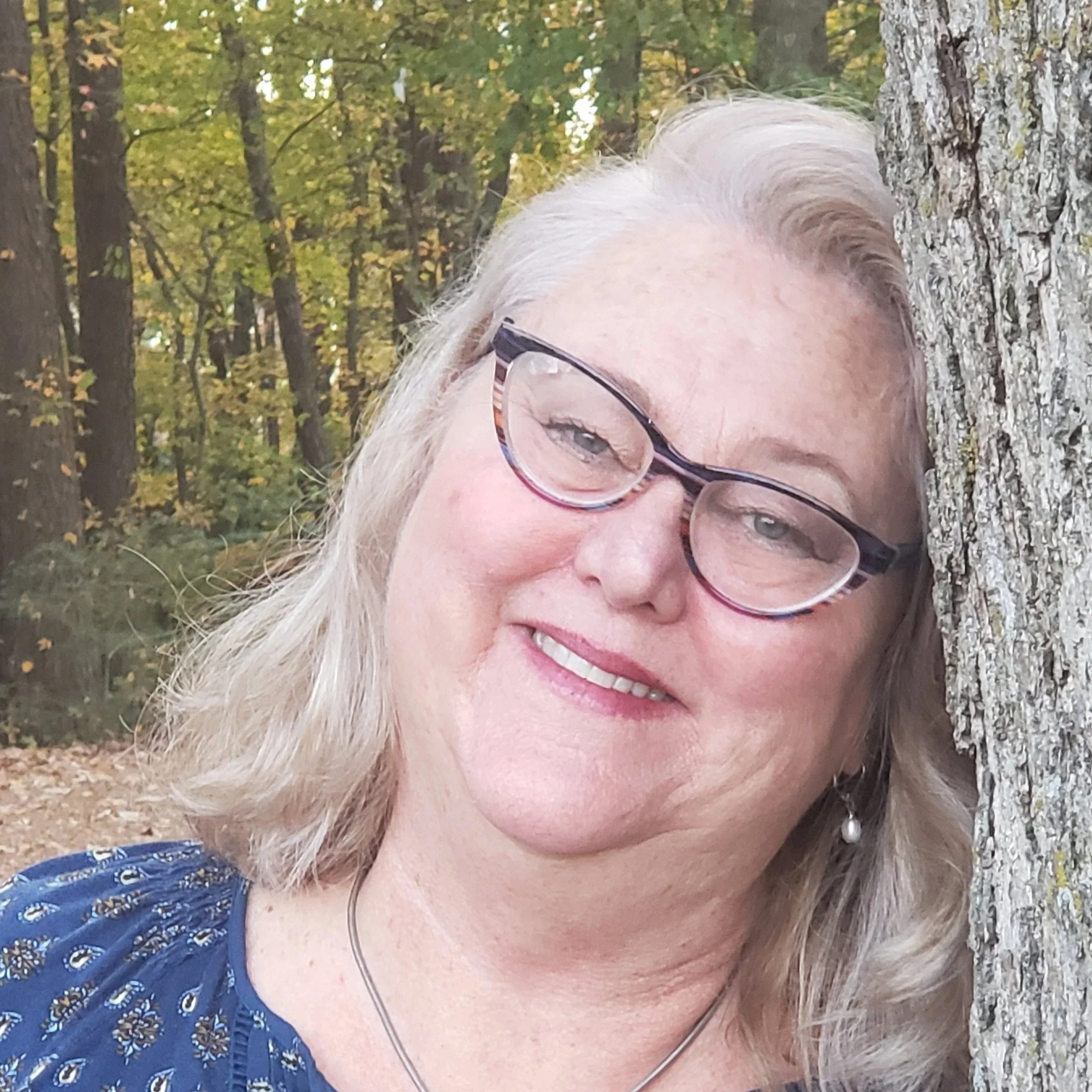 Kassie Welch standing beside a tree in a peaceful forest setting, conveying calm and grounding.