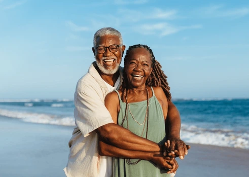 Joyful older African American couple embracing on the beach, reflecting long‑term connection and companionship.