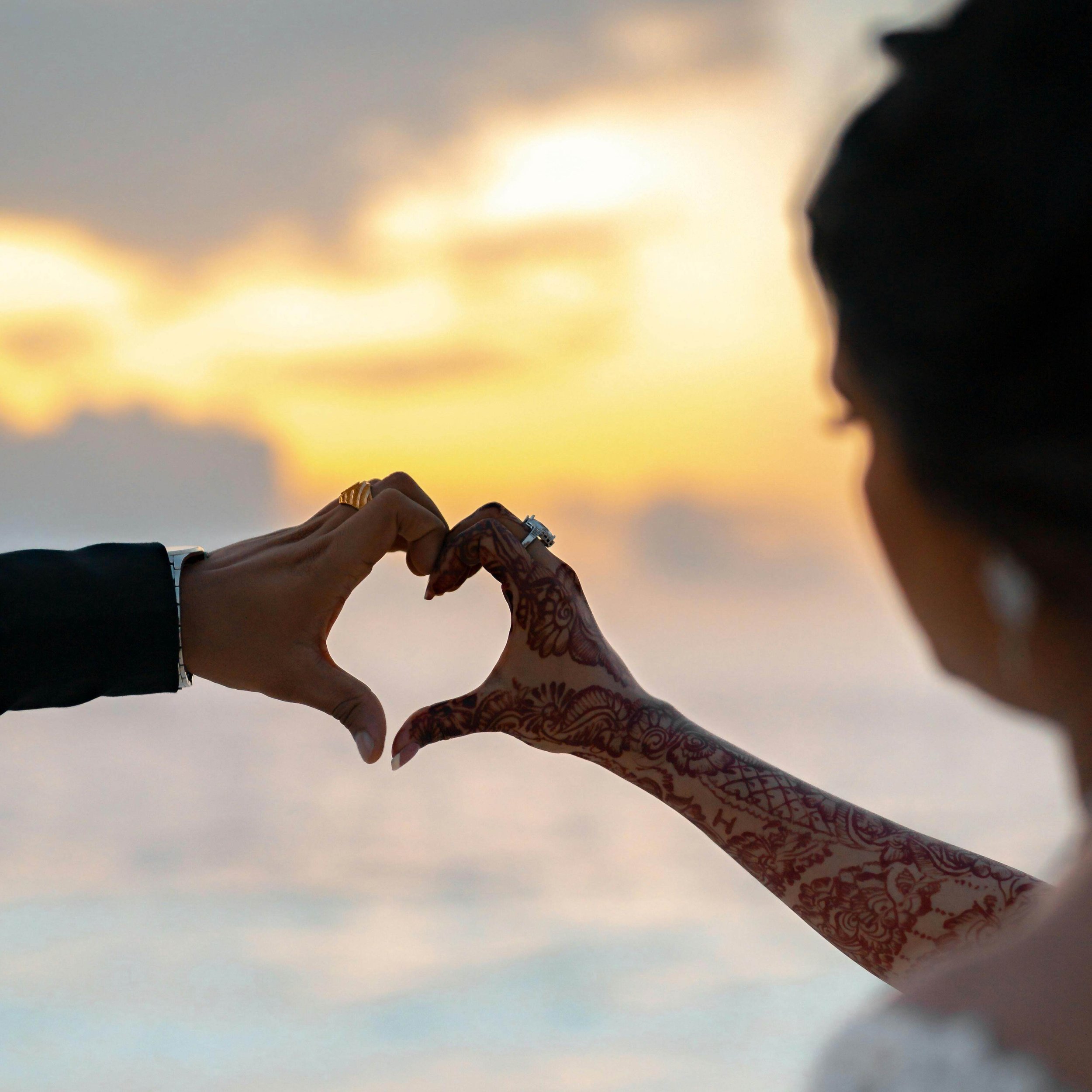 Hands forming a heart at sunset, representing connection, commitment, and relationship healing.