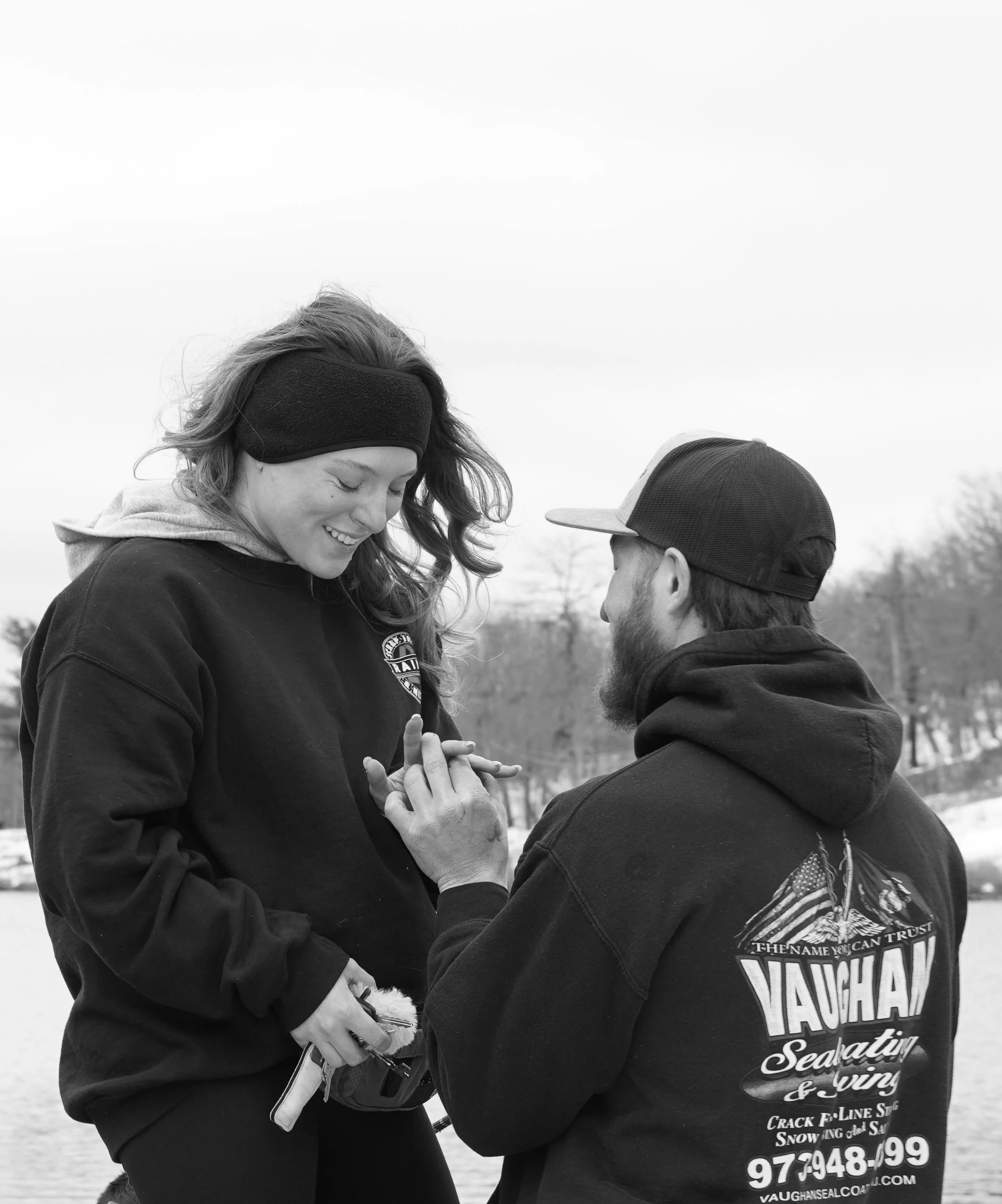 A man proposing marriage to a woman outdoors by a lake in winter, both smiling and holding hands. Engagement photography northern nj
