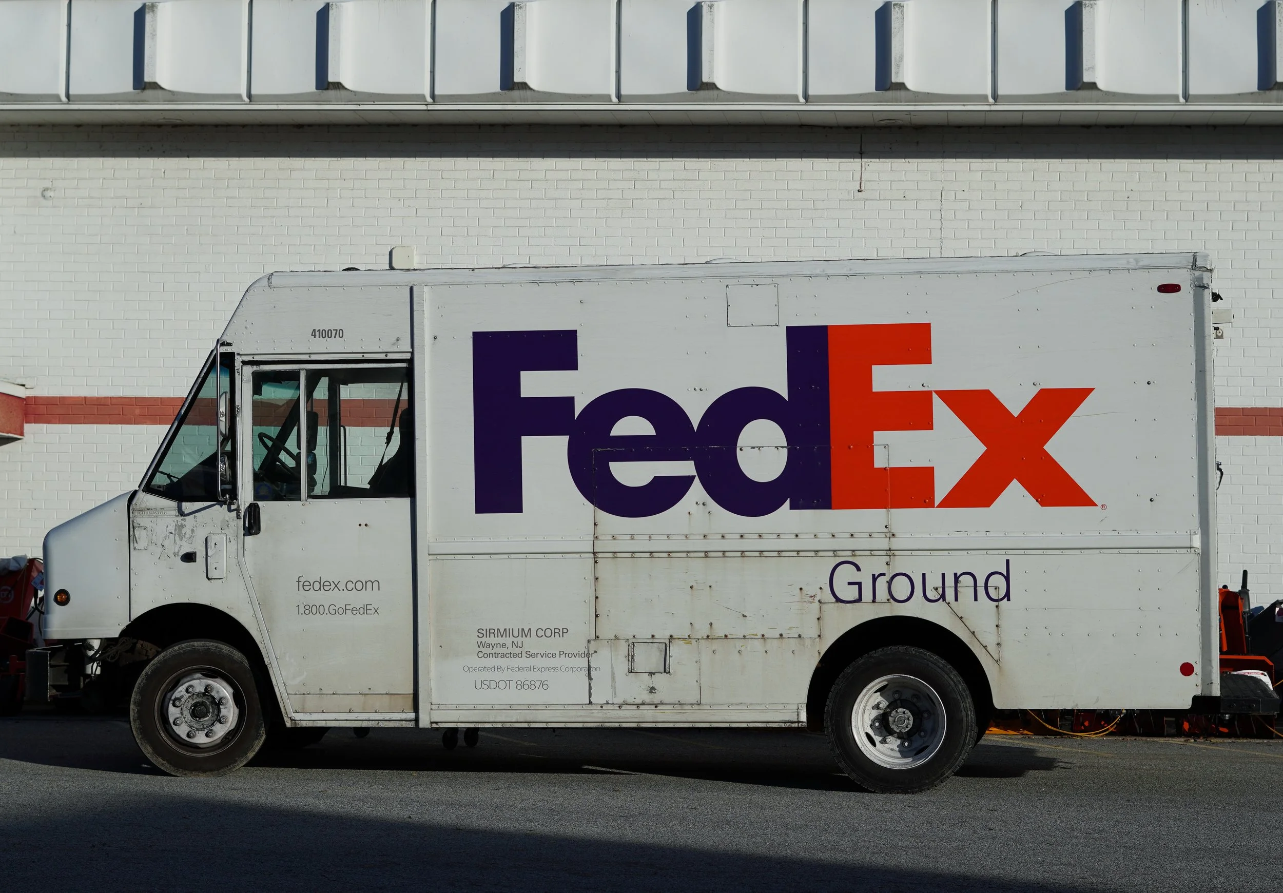 FedEx delivery truck parked in front of a white brick wall with red and blue accents. cheap business photographer northern nj