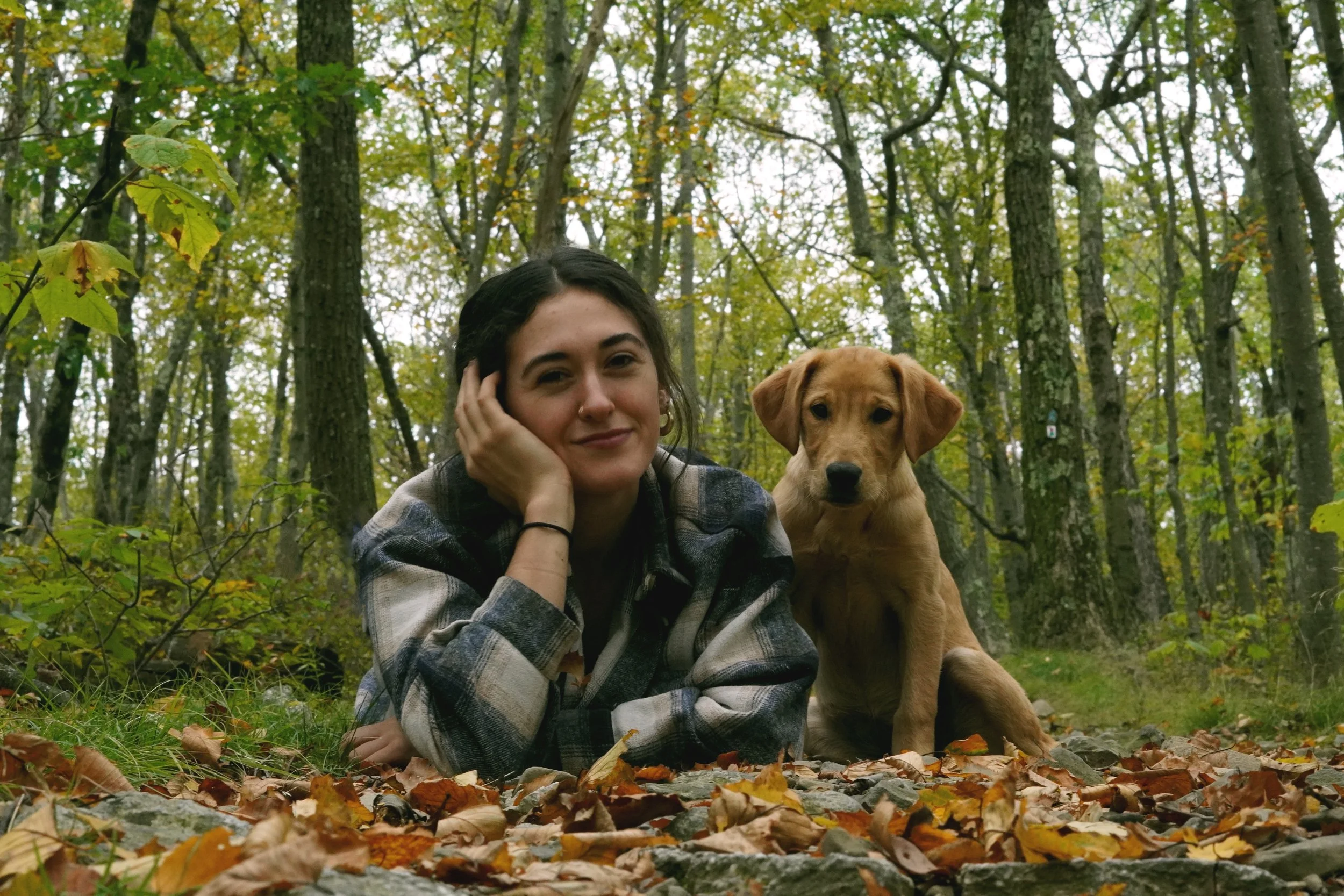 A woman and a dog lying on the ground covered with fallen autumn leaves in a forest. Vintage dog photographer northern nj