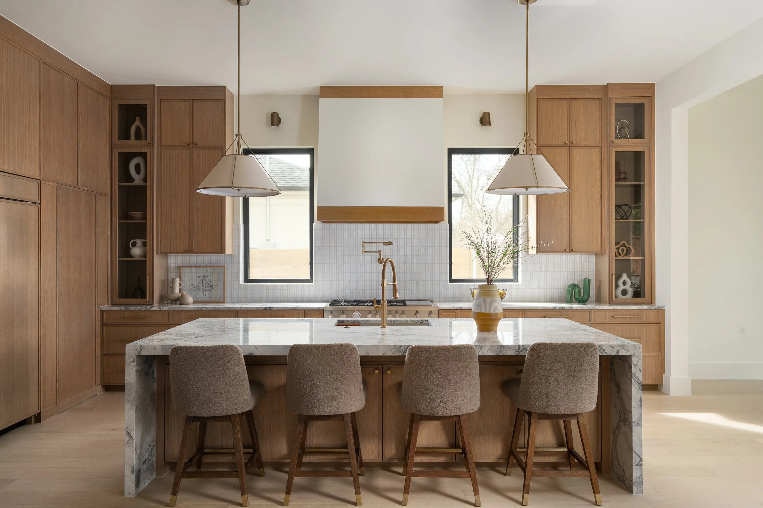 Modern kitchen with wood cabinets, white marble island, pendant lights, and large windows with a view of the outdoors.