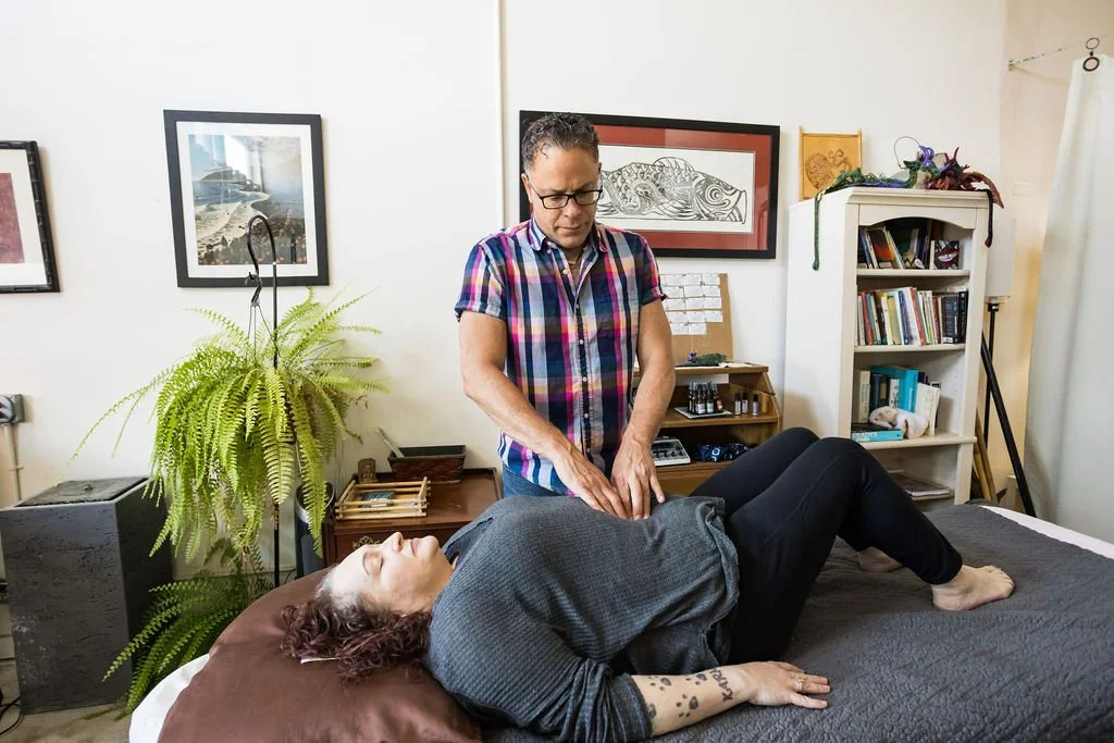 A person receiving a therapeutic treatment from a practitioner in a cozy, well-decorated room with framed artwork, books, and a large plant.