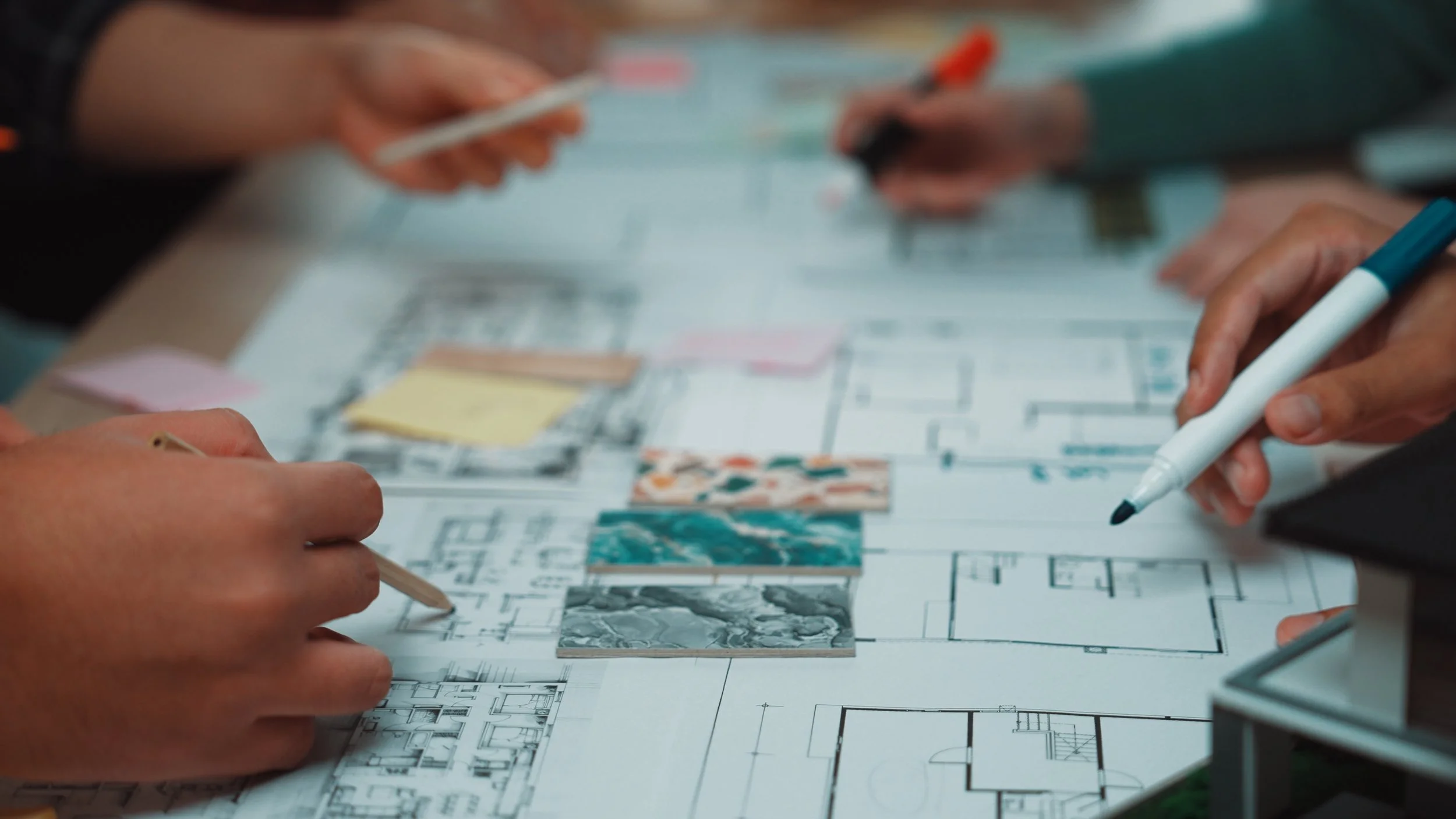 People working on architectural plans with markers and color swatches on the table.