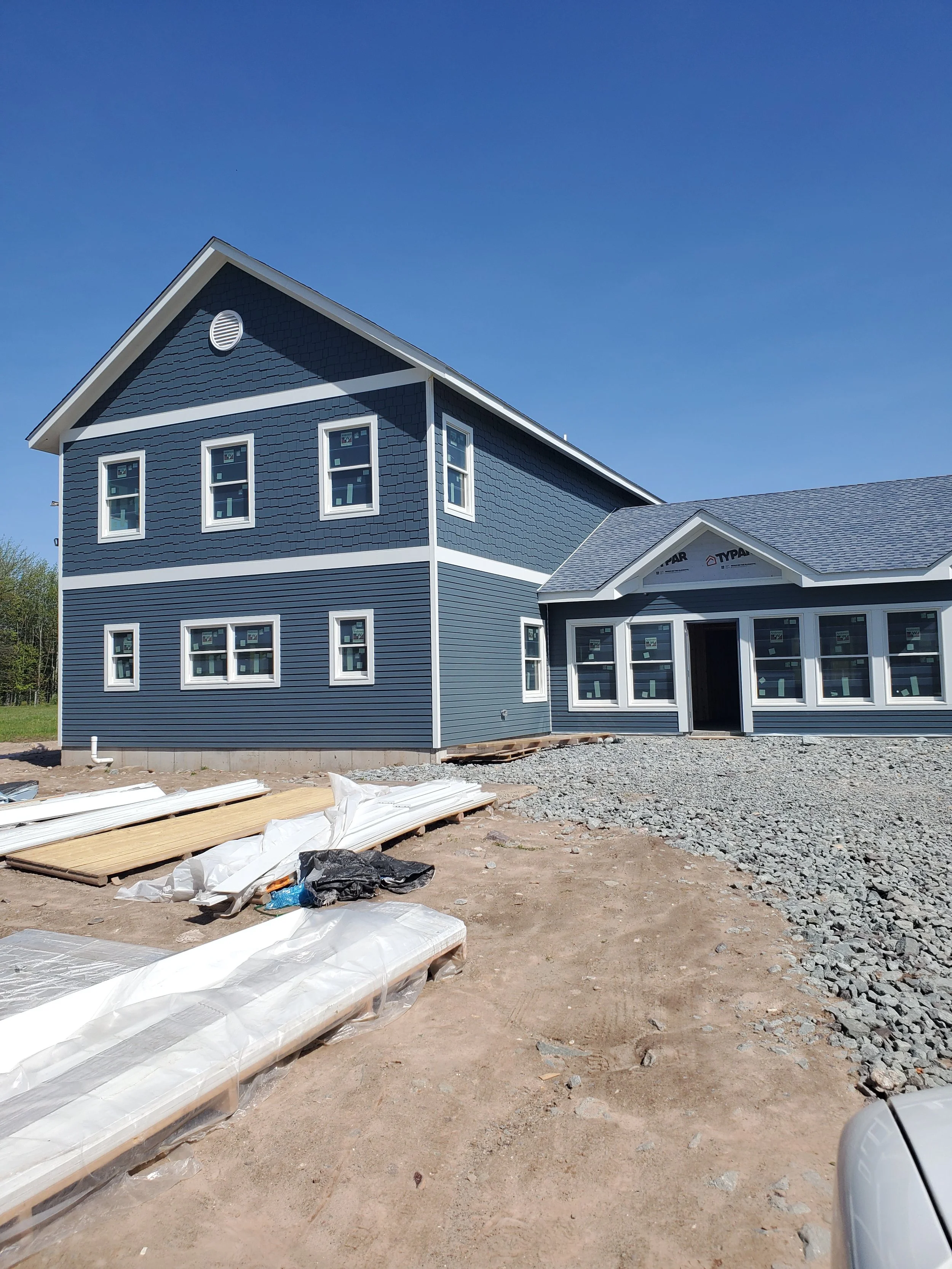 New blue house under construction with multiple windows and a gravel driveway