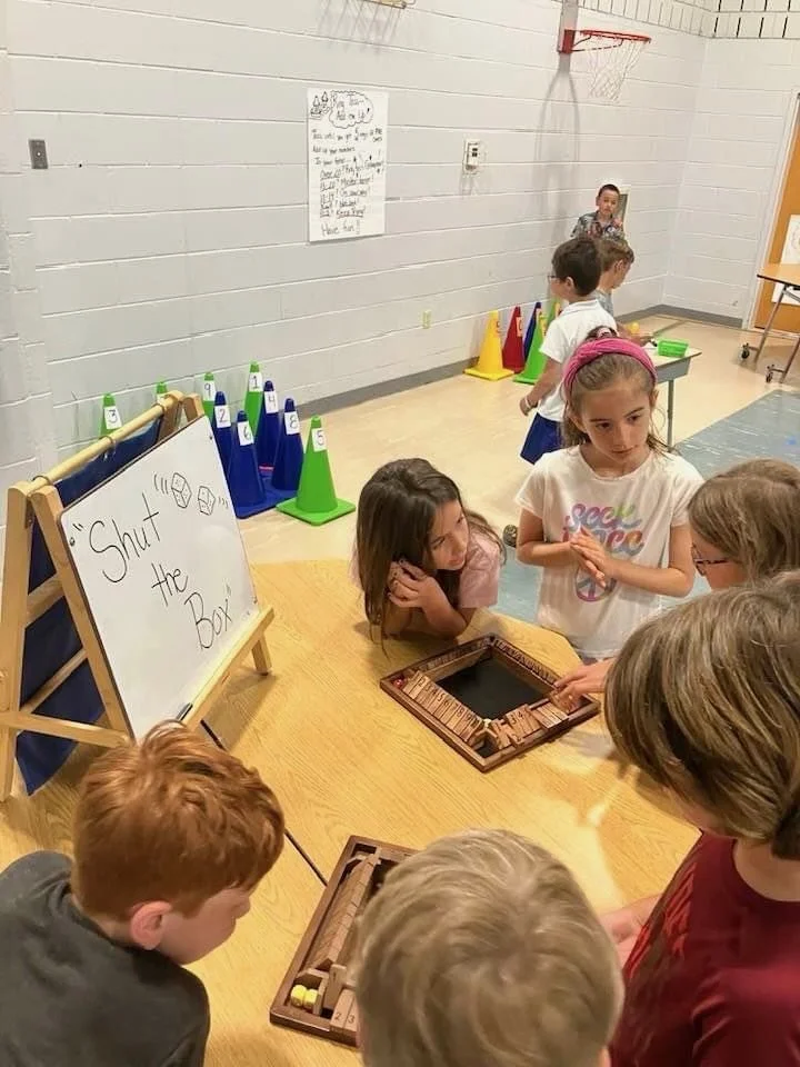 Children playing a game of Shut the Box in a school gymnasium.
