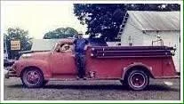 Vintage pink pickup truck parked on a grassy area with a person standing beside it