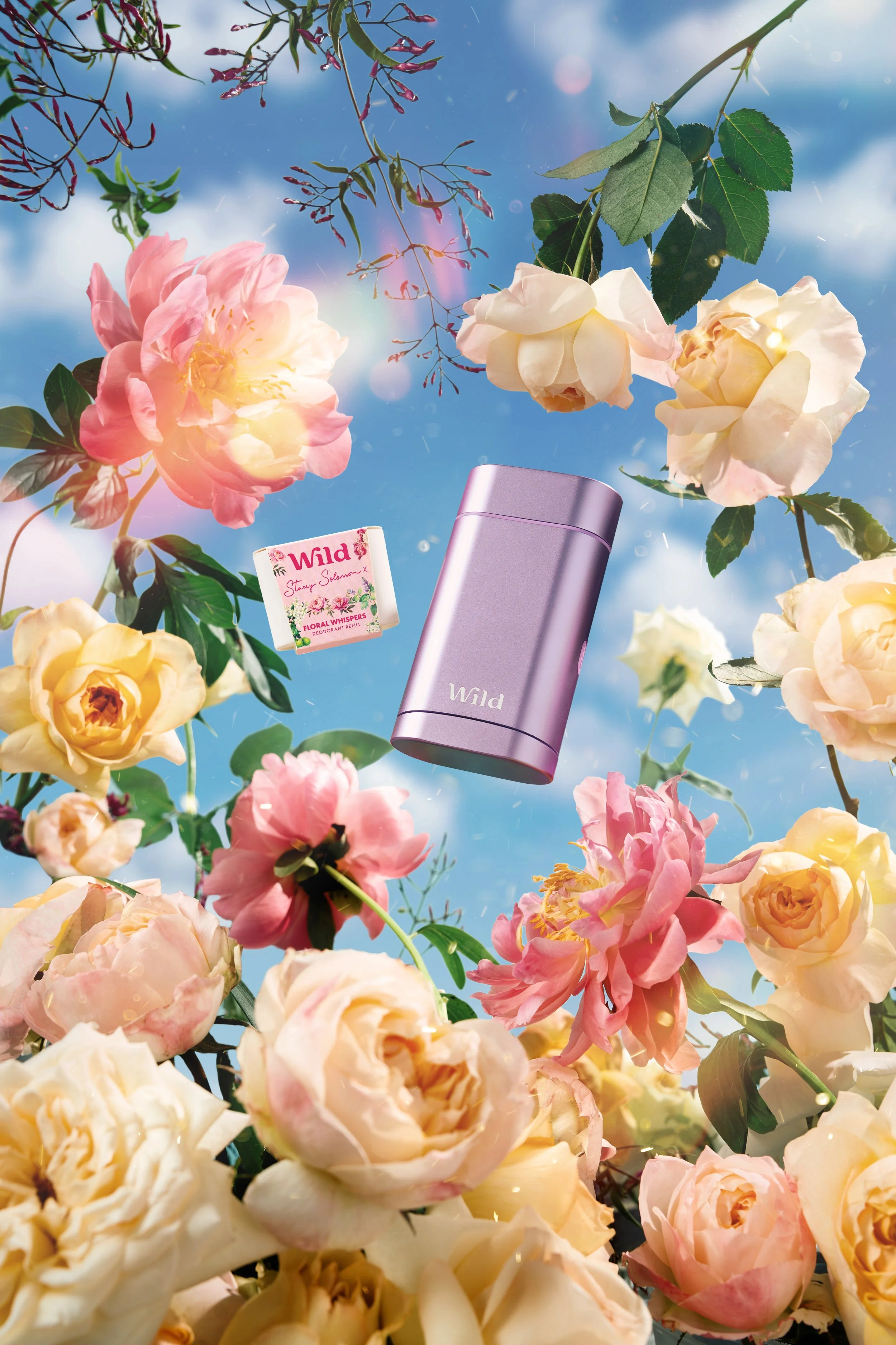 A spray of pink, peach, and yellow roses and blossoms floating in the sky with sunlight and clouds, featuring a purple Wila deodorant container and a small box of Wild floral whispers.