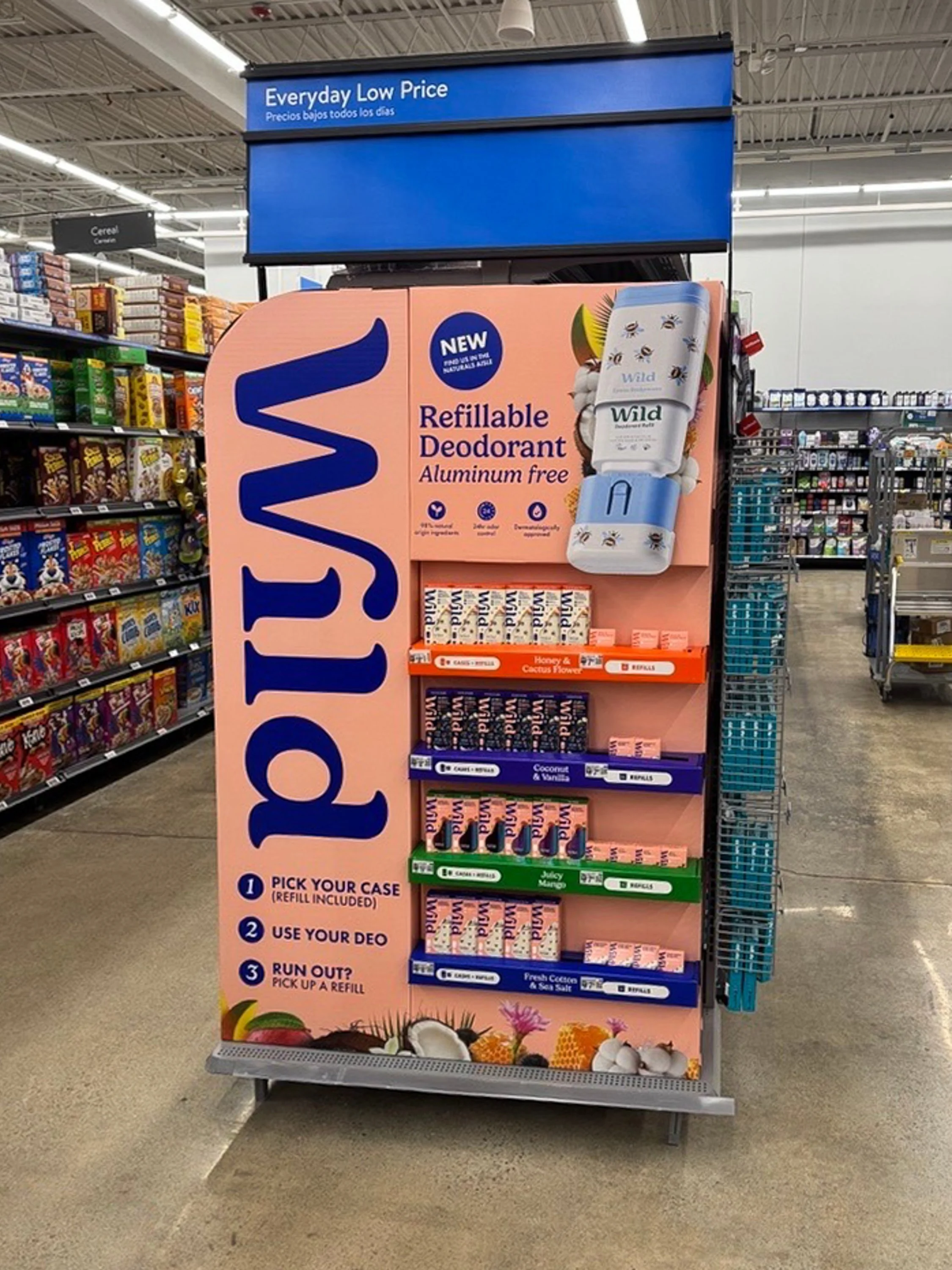Display stand for Wild brand refillable deodorant with a hanging container of deodorant, featuring some products with floral and tropical themes. The sign emphasizes the deodorant is aluminum free, with options for various scents, and provides instructions for using the product.