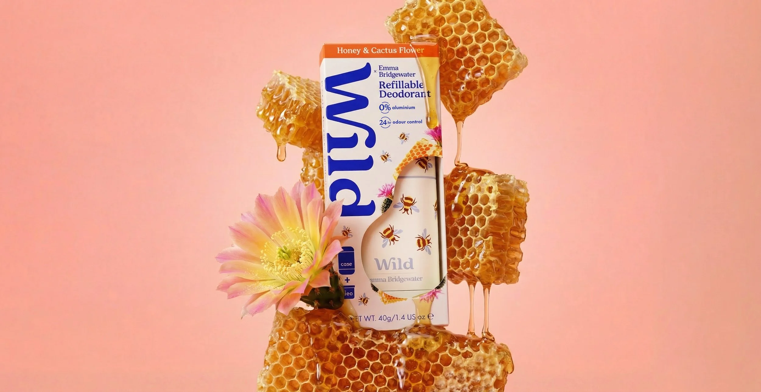 A promotional display featuring a honey and cactus flower scented refillable deodorant by Emma Bridgewater. The deodorant is surrounded by honeycomb pieces, with honey dripping from them, and a pink flower next to the product. The background is a soft pink.