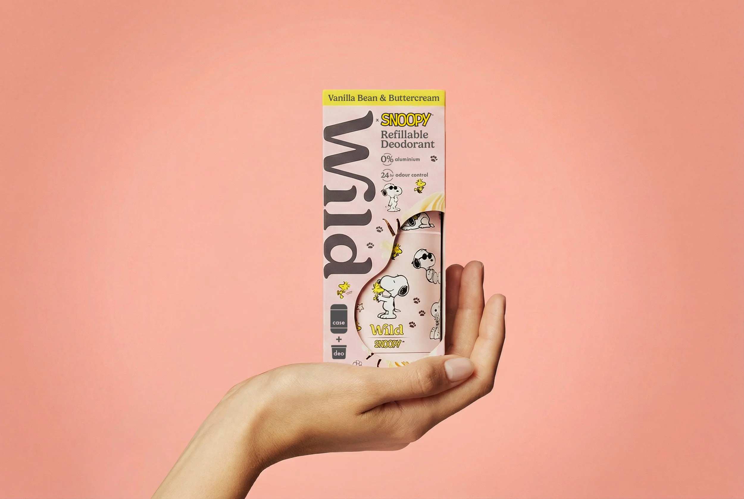 Hand holding a Peanuts-themed Snoopy refillable deodorant container against a pink background.