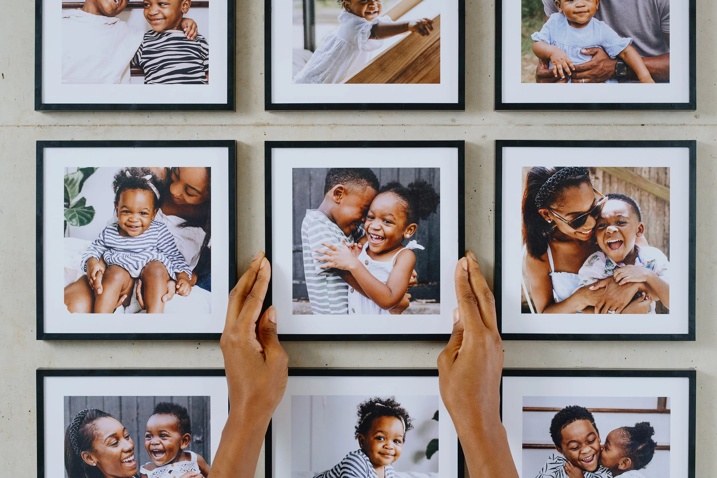 Person arranging framed photographs of children and families on a wall.
