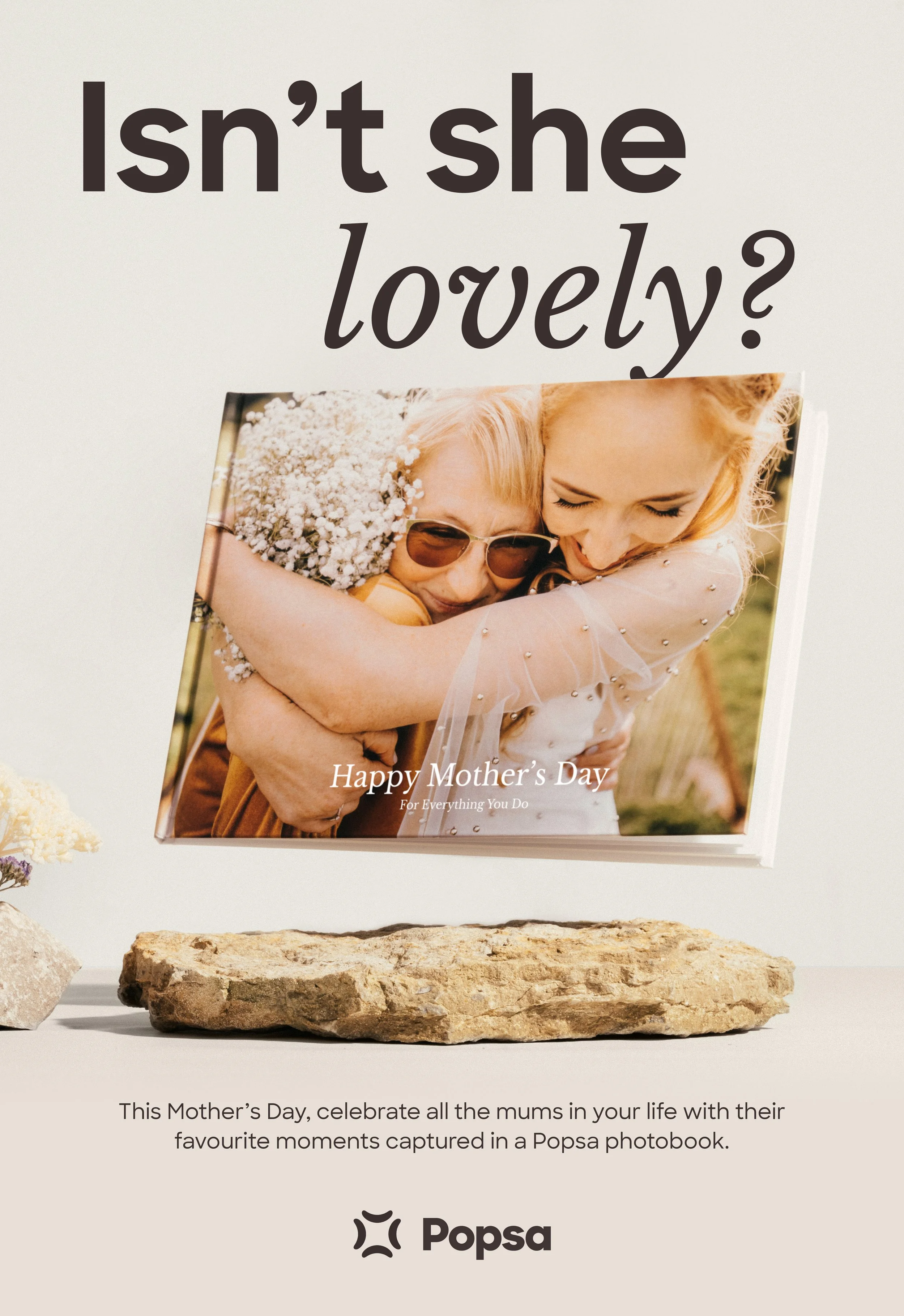 A promotional image for Mother's Day showing a photo book with a picture of two women hugging, one wearing sunglasses and the other with red hair. The text above the book reads, "Isn’t she lovely?" and the caption below states, "This Mother’s Day, celebrate all the mums in your life with their favorite moments captured in a Popsa photobook."