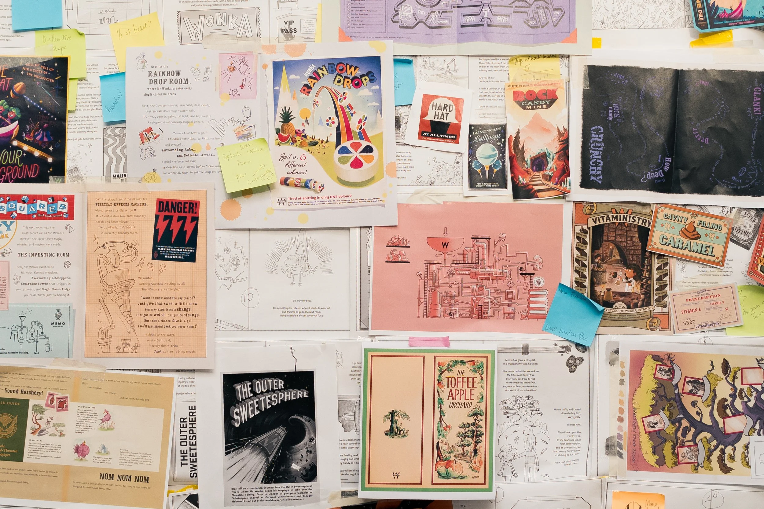 A collage of various colorful paper pieces, some with printed text, illustrations, notes, and sketches, attached to a wall, creating a busy, creative bulletin board.