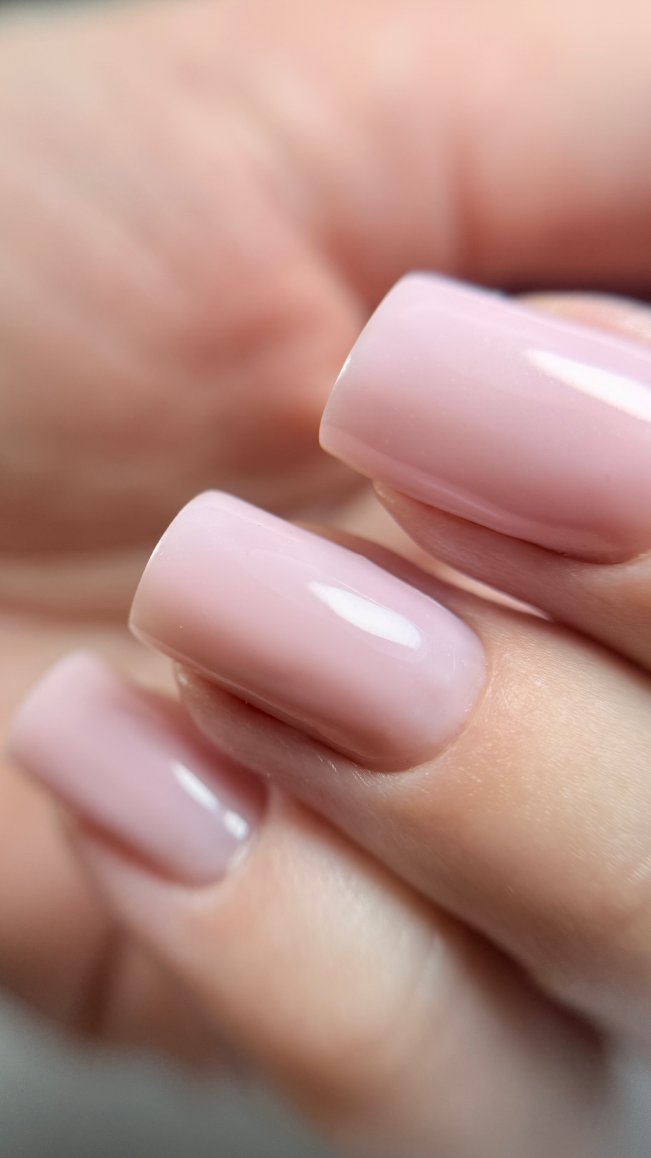 Close-up of neatly manicured fingernails painted in light pink polish.