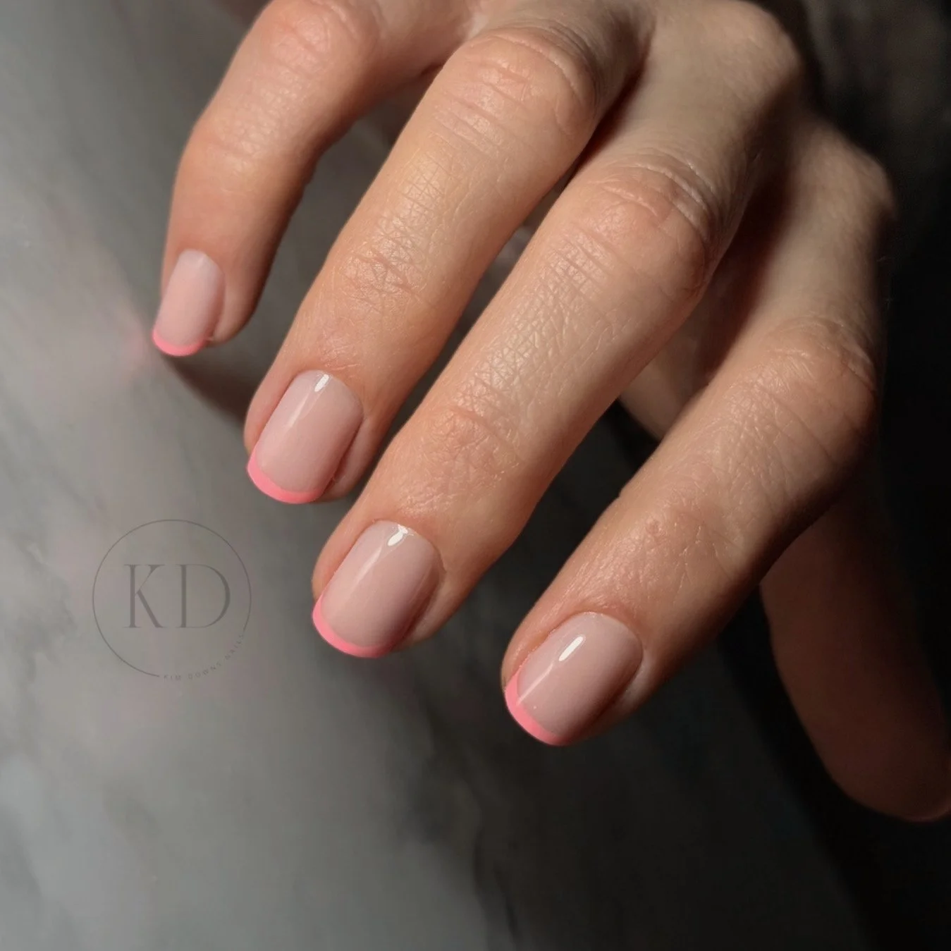 Close-up of a person's hand with well-manicured nails painted in nude with pink tips.