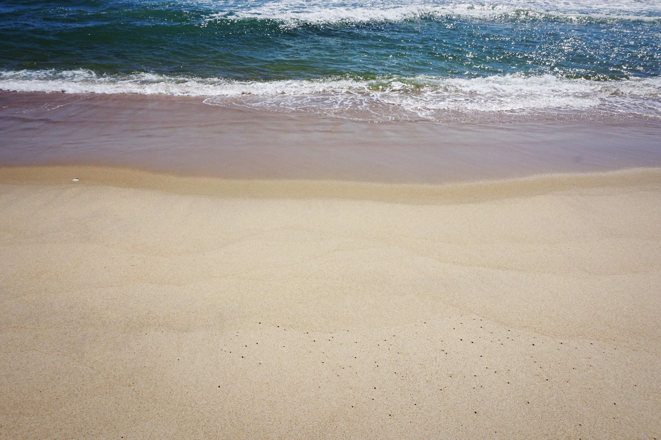 Sunny beach with light-colored sand and gentle waves rolling in from the ocean.