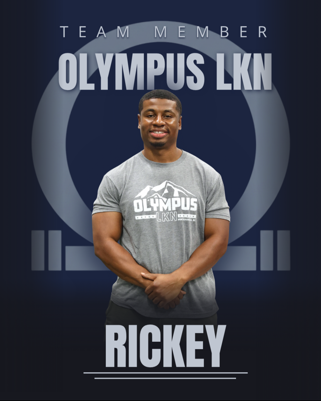 A smiling man wearing a black t-shirt with a logo, standing in a gym with exercise equipment and a blue banner in the background.