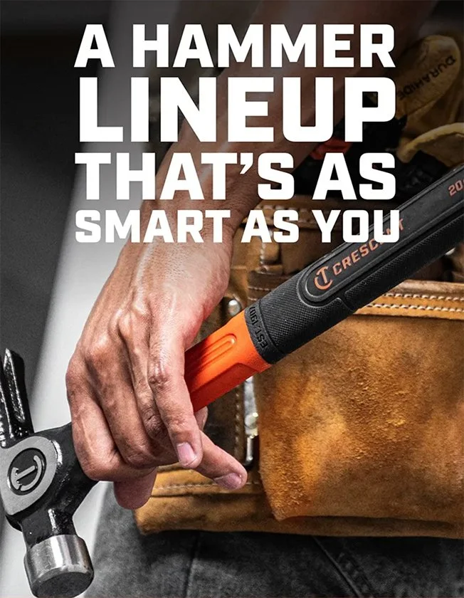 Close-up of a hand holding a hammer lined up with a tool with a smart display. The background shows part of a person wearing brown work gloves and a brown work apron.