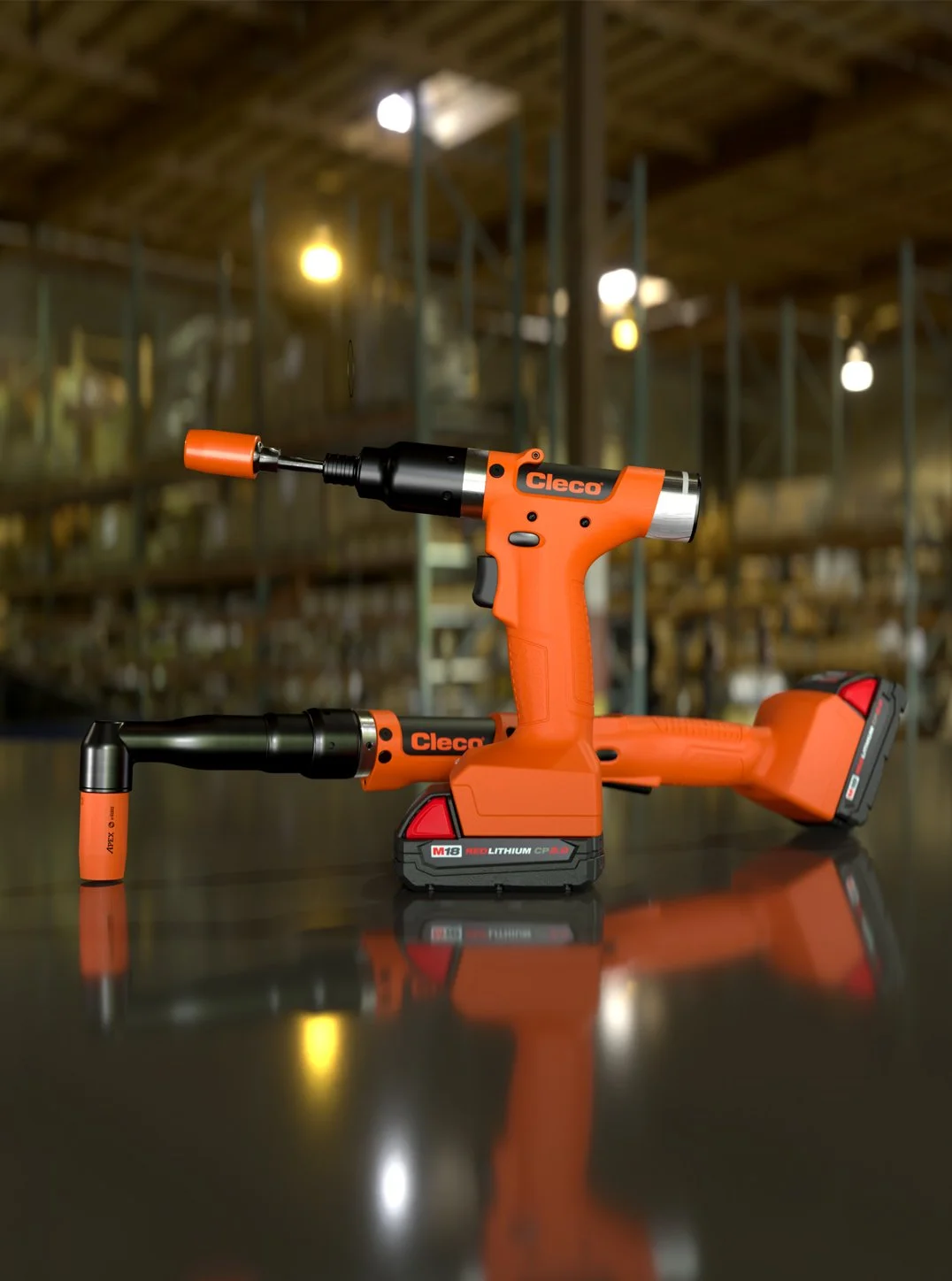 Orange cordless power tools, a drill and an impact wrench, with a black and red battery pack, on a reflective surface in a warehouse setting.